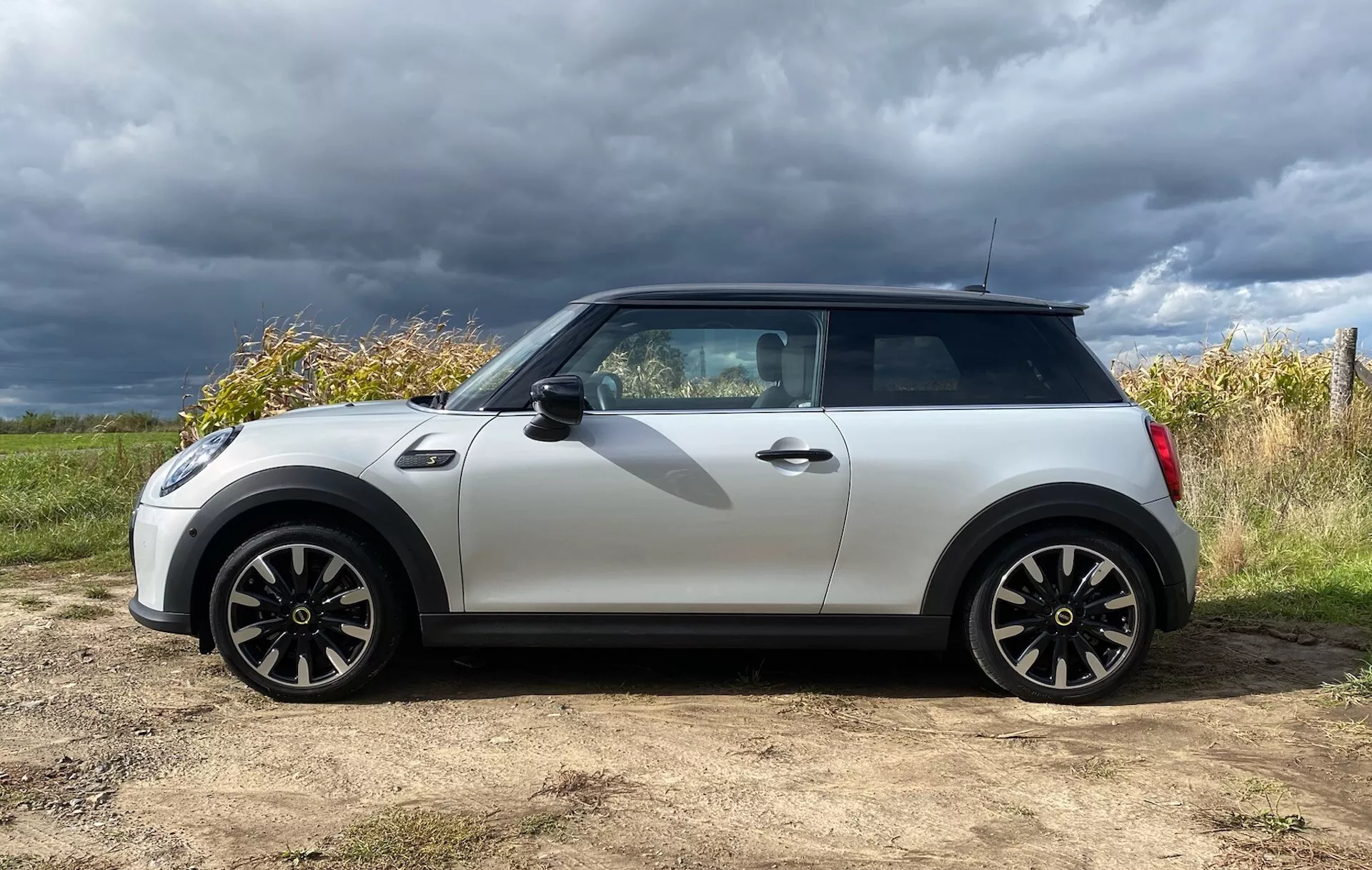 Mini Cooper Électrique 3 Portes 2021 en Blanc et Noir, avec Roues Sport et Accès sans Clé, Devant un Ciel Couvert et un Paysage Naturel