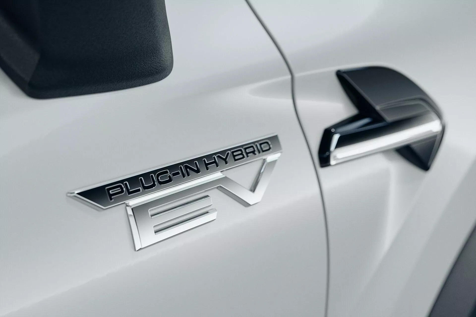 Gros plan du côté de la voiture blanche Mitsubishi ASX 2023 de deuxième génération, avec badge 'PLUG-IN HYBRID EV' proéminent, rétroviseur latéral noir élégant avec clignotant intégré et carrosserie aérodynamique blanche brillante.