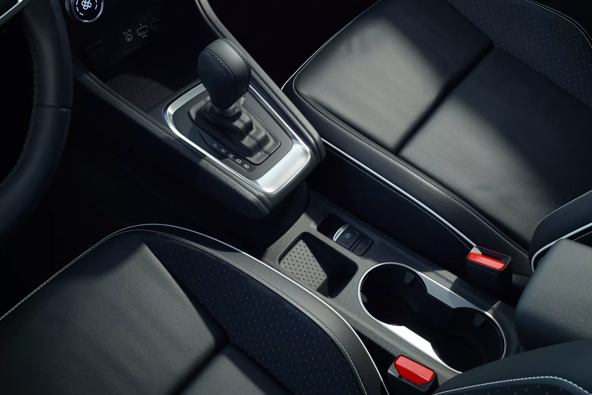 Photo intérieure vue du dessus de la console centrale de la Mitsubishi ASX 2023 deuxième génération, avec des détails comme le levier de vitesse en cuir, des accents chromés autour de la zone des changements de vitesse, un compartiment de rangement avec plateau amovible, deux porte-gobelets à bords chromés, des sièges en cuir noir avec des coutures visibles, le bouton de frein de parking électronique et l'accoudoir central partiellement visible, montrant des matériaux de haute qualité et un design moderne.
