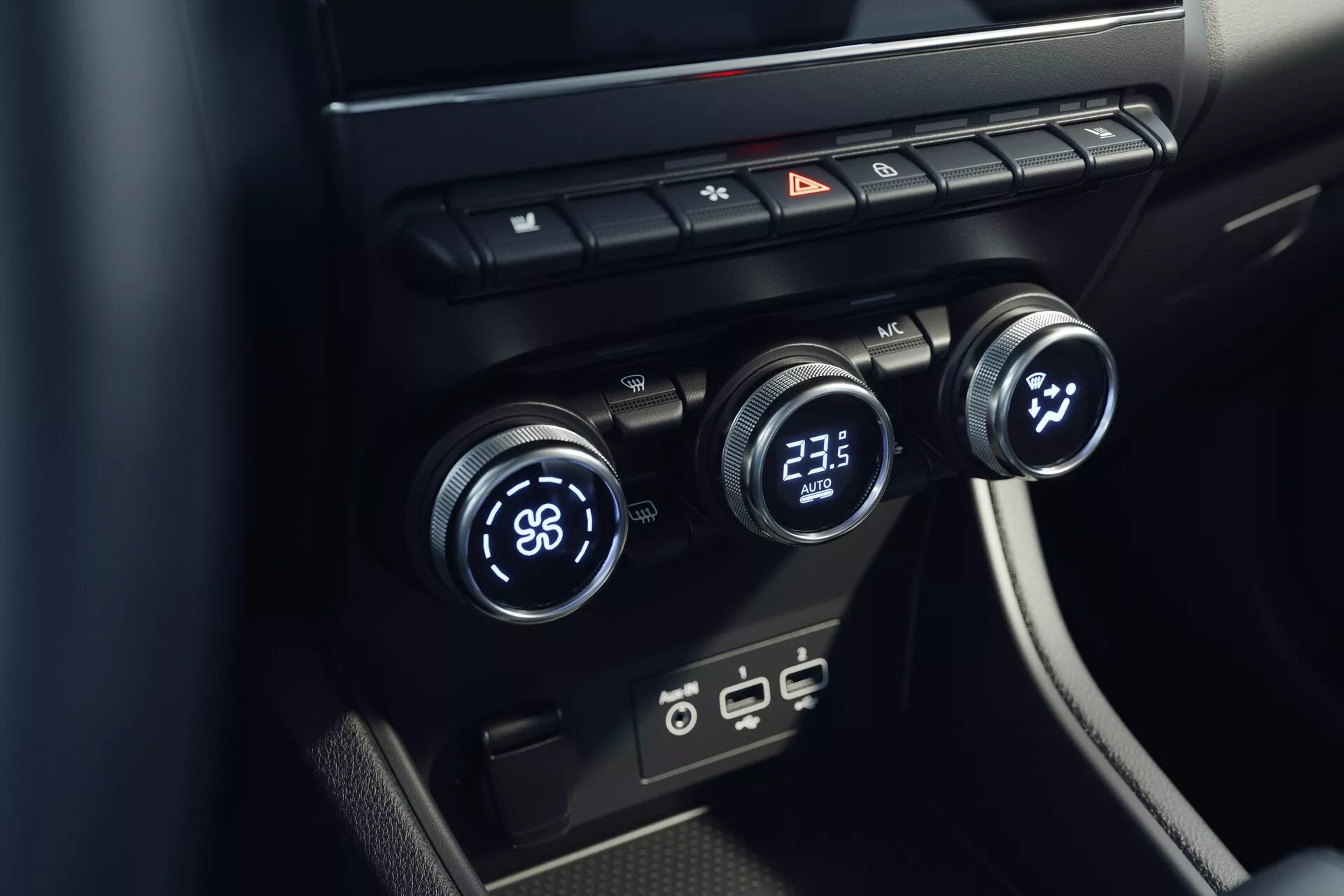 Vue rapprochée du système de contrôle du climat intérieur de la Mitsubishi ASX 2023 (2e génération). L'image, prise d'un angle surélevé, se concentre sur la console centrale avec trois commandes de température : la gauche réglée sur 'LO' et la droite sur '23.5'. Le cadran central semble contrôler la vitesse ou la direction du ventilateur. Au-dessus, des boutons pour le dégivrage, les feux de détresse et la circulation d'air. En dessous, des ports USB modernes. Le design est minimaliste avec des surfaces noires élégantes.