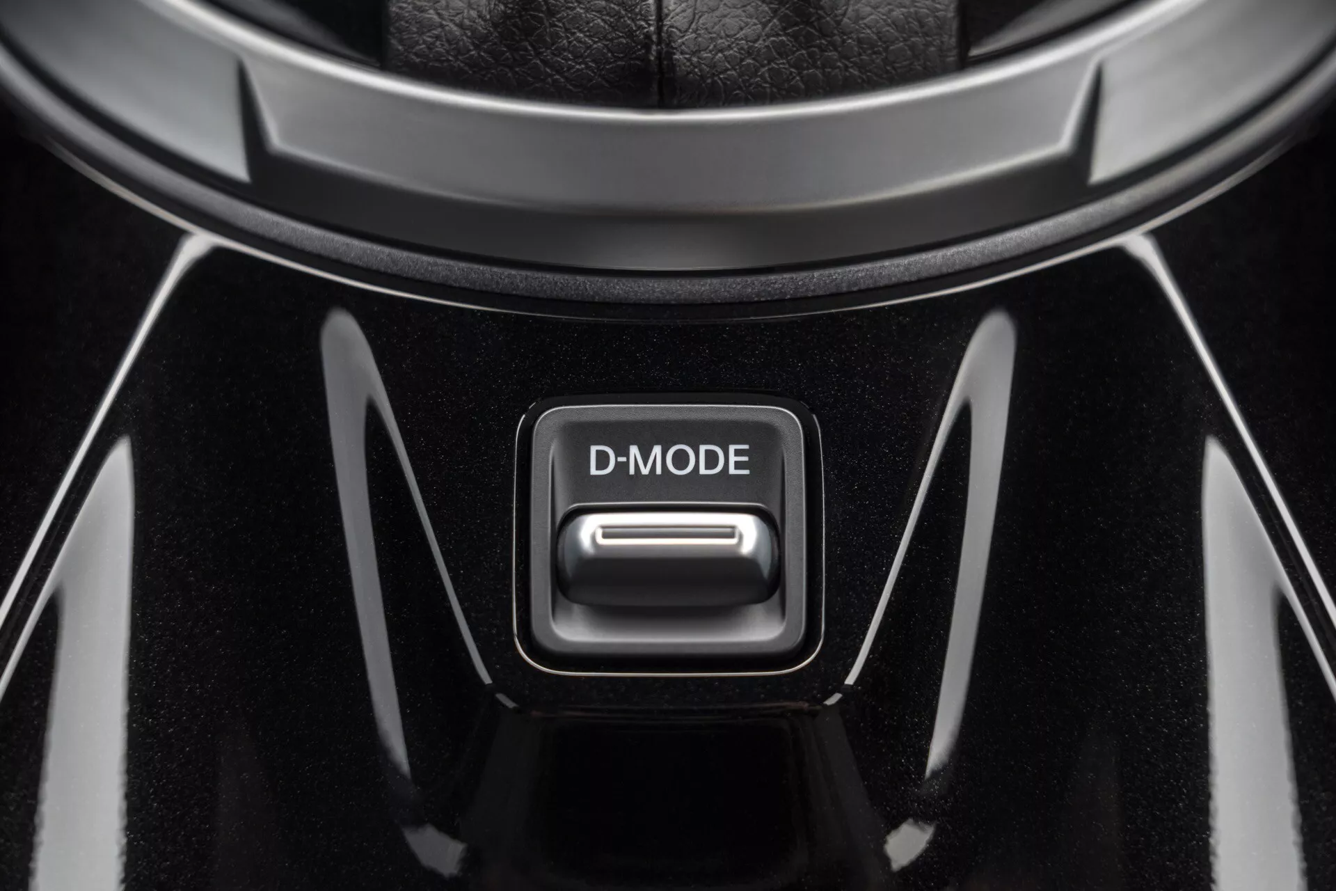 Vue rapprochée du bouton D-MODE sur la console centrale d'une Nissan Juke 2019 (F16), présentant une finition noire brillante avec des accents chromés sous un éclairage plongeant