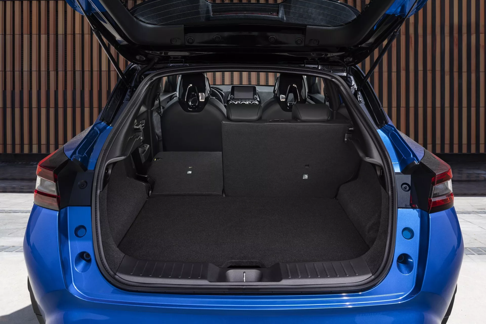 Nissan Juke (F16) de 2019 présentant un coffre spacieux et vide avec le couvercle ouvert, vue détaillée de l'espace de chargement avec une moquette comme revêtement, encadrée par des feux arrière rouges distinctifs et des caractéristiques de design extérieur moderne, depuis une perspective arrière directe.