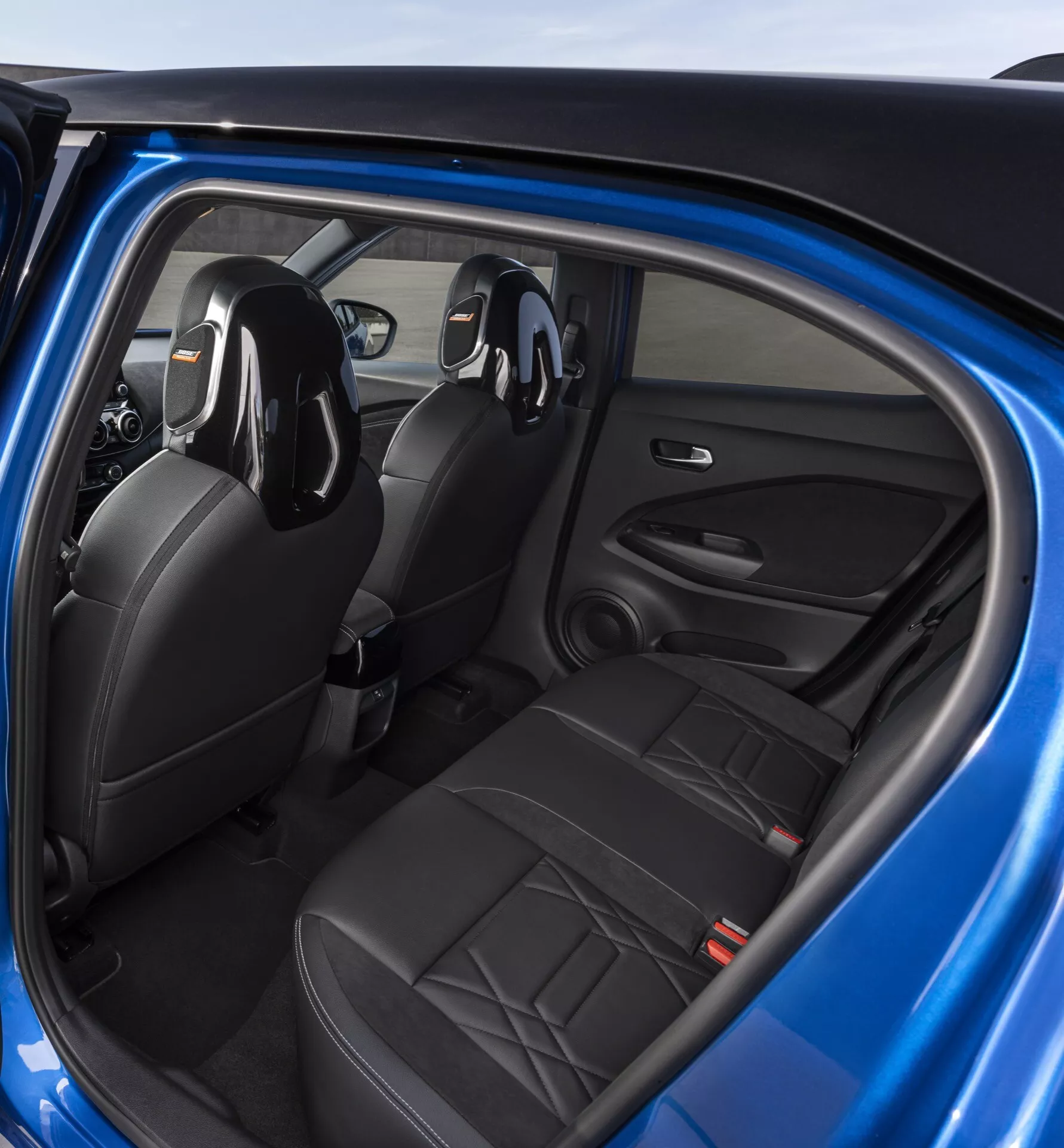 Vue intérieure du Nissan Juke 2019 (F16) depuis la perspective du passager arrière présentant des sièges en cuir noir, des commandes sur la porte du conducteur et un système audio intégré