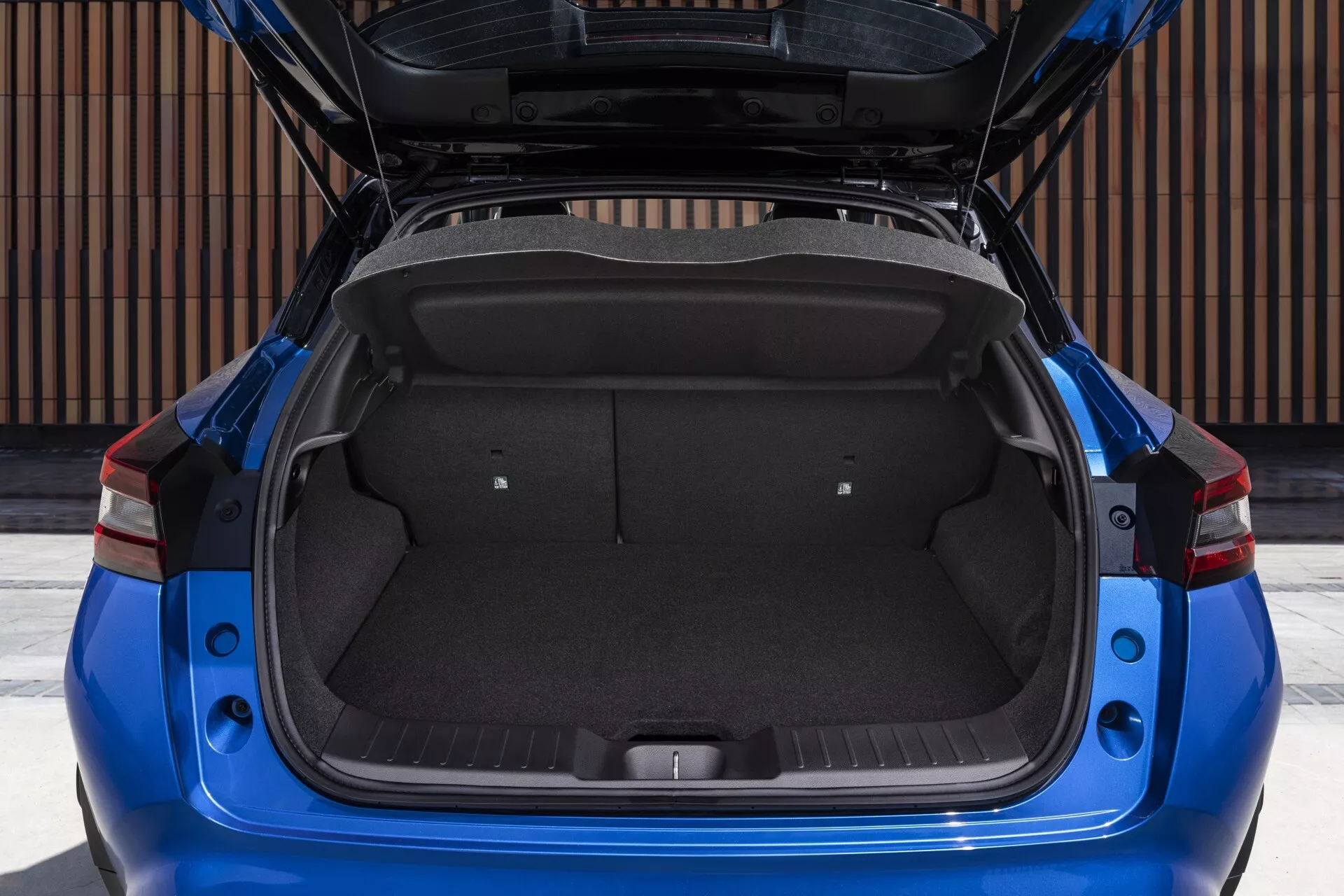 Vue arrière directe d'un Nissan Juke 2019 (F16) mettant en évidence l'espace de chargement spacieux du coffre ouvert, présentant un intérieur propre et bien entretenu avec tapis standard et espace de rangement maximisé en raison des sièges arrière rabattus. Le design moderne du véhicule est accentué par des feux arrière LED aigus et angulaires et un pare-chocs arrière de couleur carrosserie, indiquant un accent sur la praticité et le style.