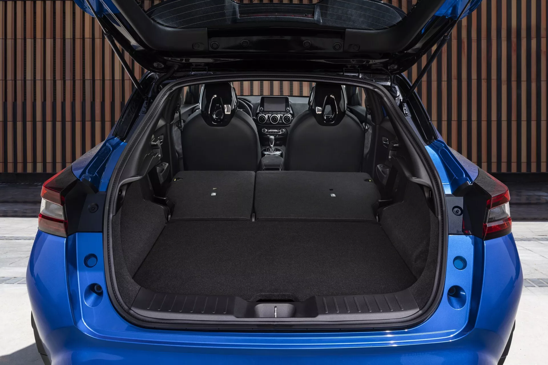 Nissan Juke F16 de 2019 en bleu, vue arrière avec hayon ouvert montrant un grand espace de chargement, sièges arrière rabattables divisés et couvercle de chargement rétractable visible