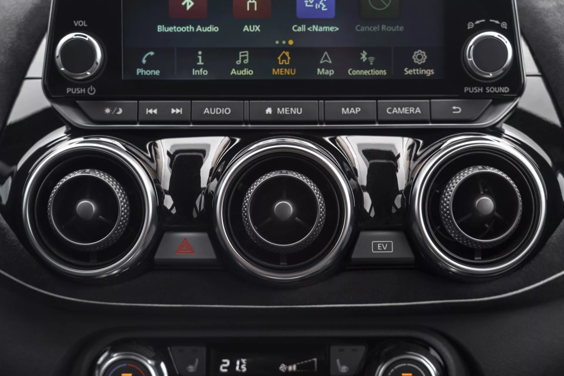 Vue détaillée de la console centrale du Nissan Juke (F16) 2019 comprenant les commandes climatiques, le système d'infodivertissement avec écran tactile incluant le mode EV, des aérateurs métalliques et le panneau de contrôle du climatiseur