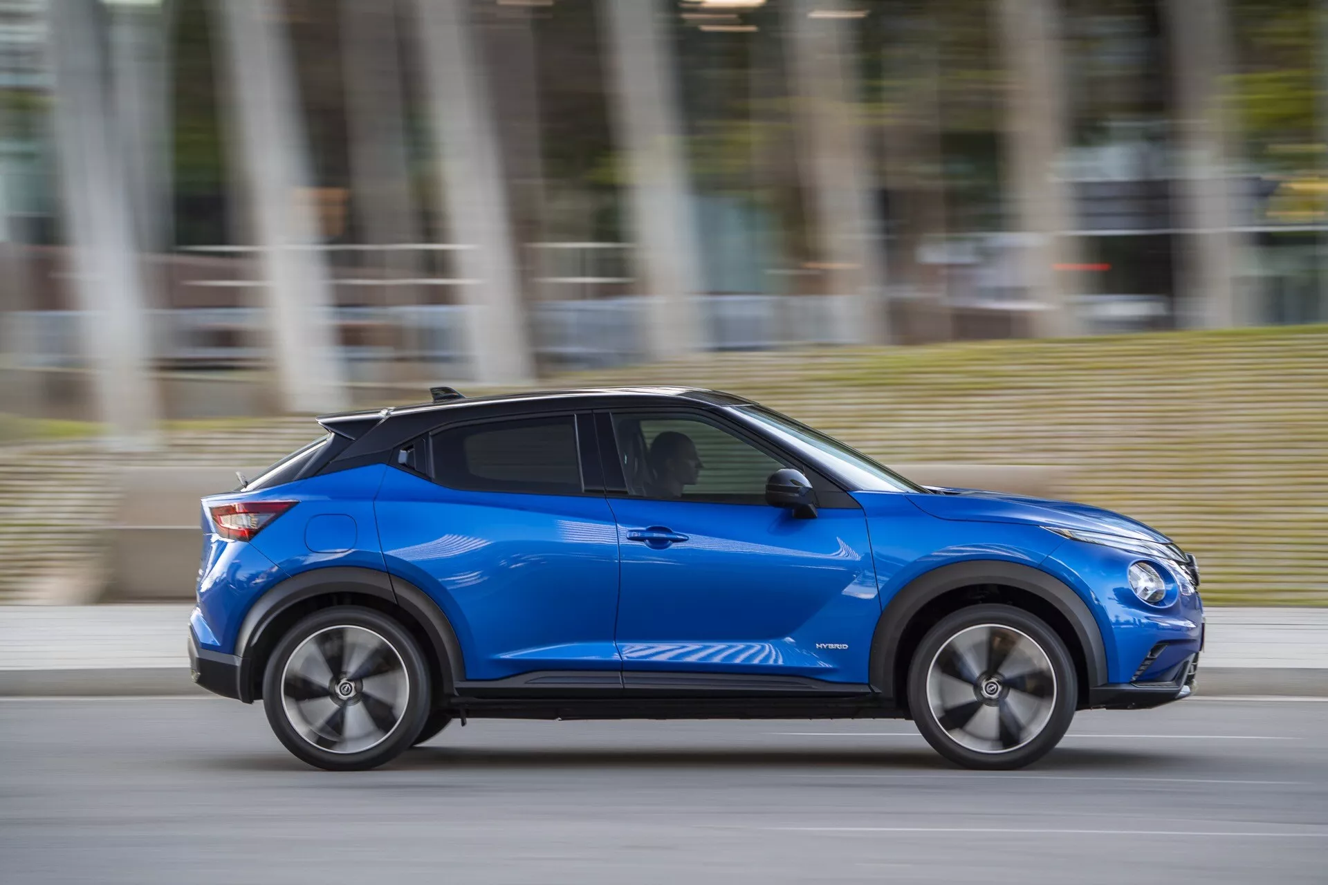 Nissan Juke (F16) 2019 en bleu, présentant un design moderne et des caractéristiques axées sur la technologie telles que des lignes de carrosserie aérodynamiques, des roues en alliage et une entrée sans clé potentielle, se déplaçant de manière dynamique avec un flou de mouvement par temps nuageux