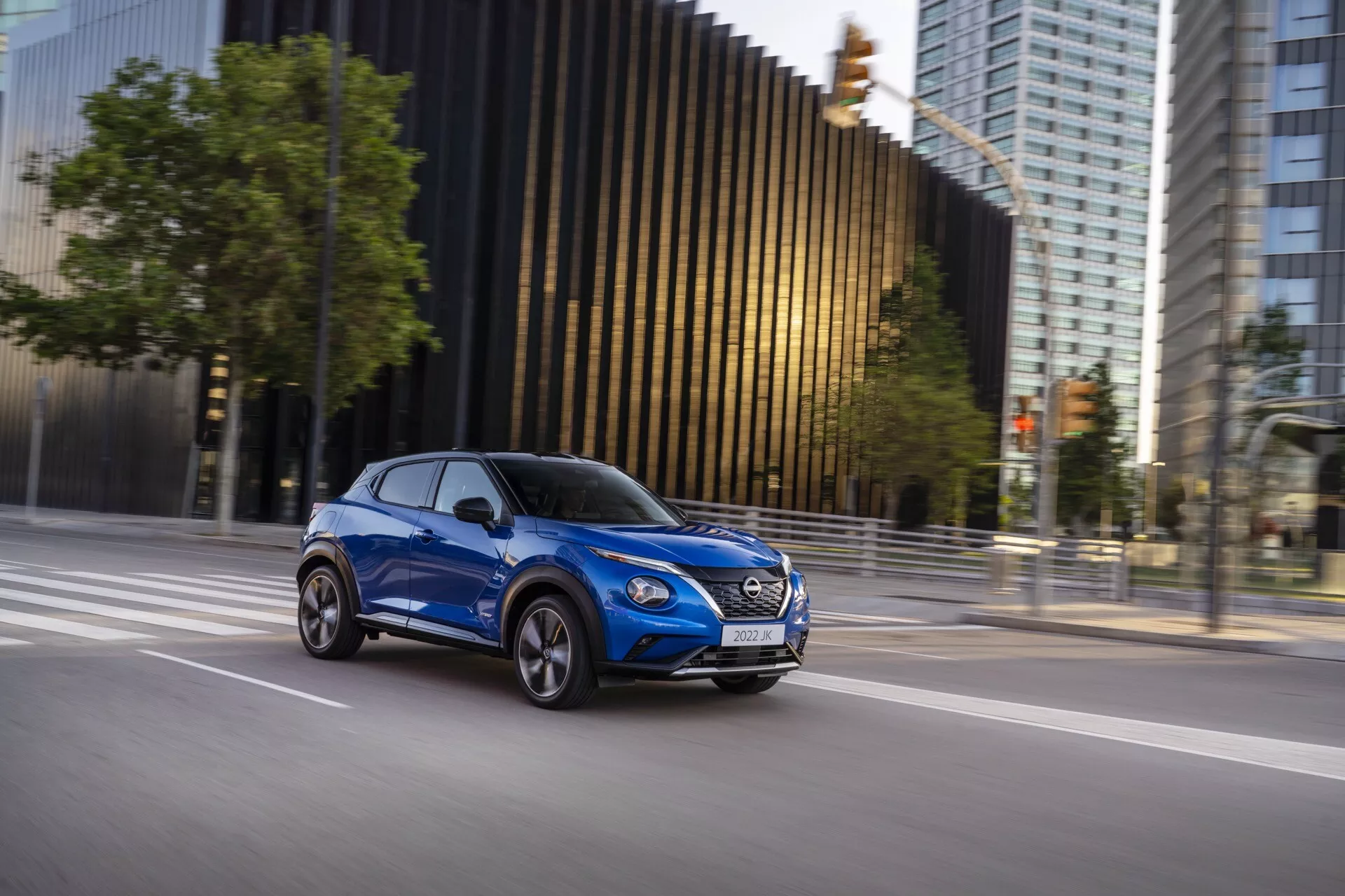 SUV compact moderne Nissan Juke (F16) de 2019 en mouvement, capturé depuis une perspective latérale en bleu vif, soulignant la conception du véhicule, la présence dynamique et les caractéristiques aérodynamiques sur un fond urbain.