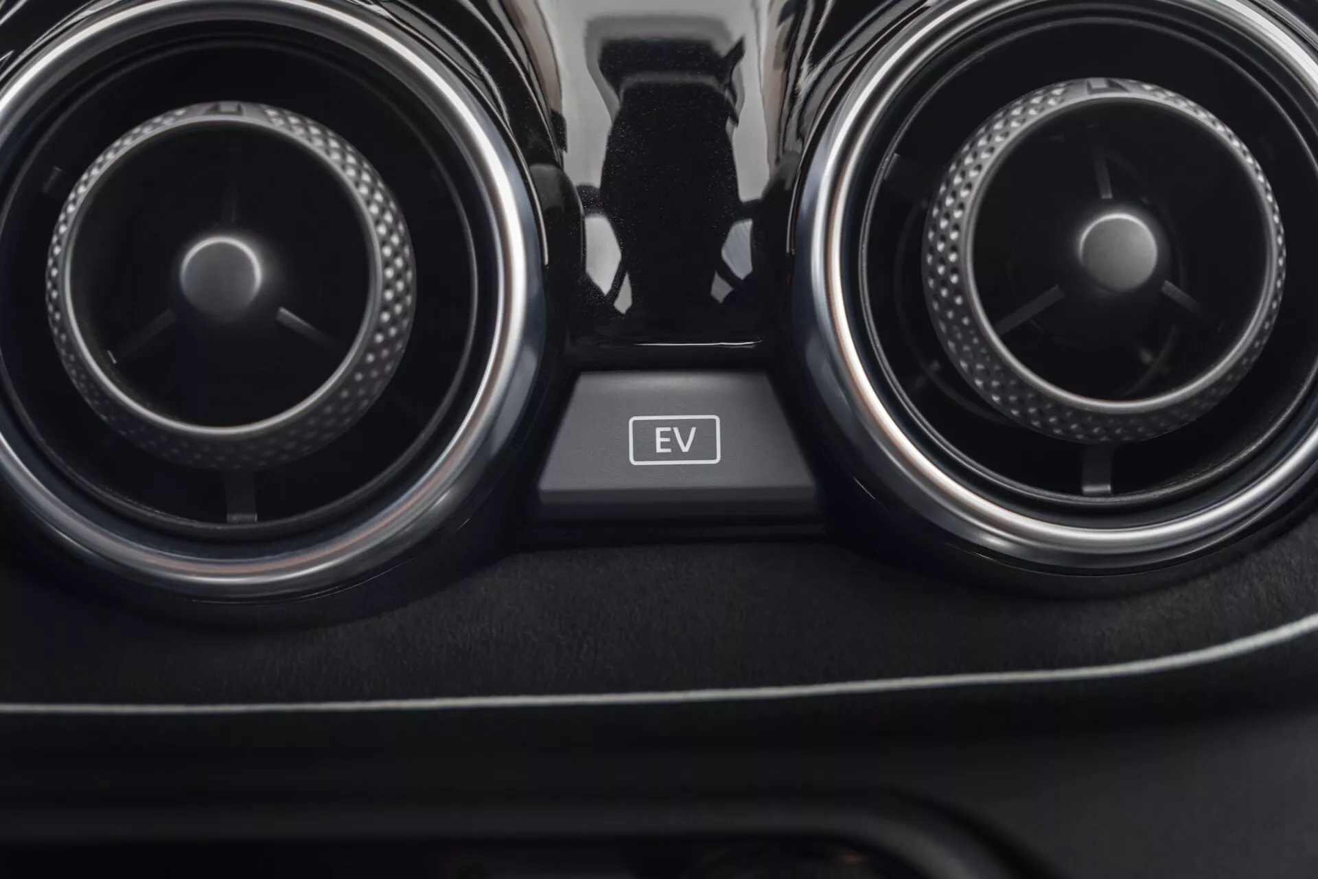 Vue rapprochée de l'intérieur de la Nissan Juke 2019 (F16) se concentrant sur les bouches d’air conditionné et le bouton du mode EV situé entre elles, mettant en avant le système de contrôle climatique de la voiture et la technologie des véhicules électriques.