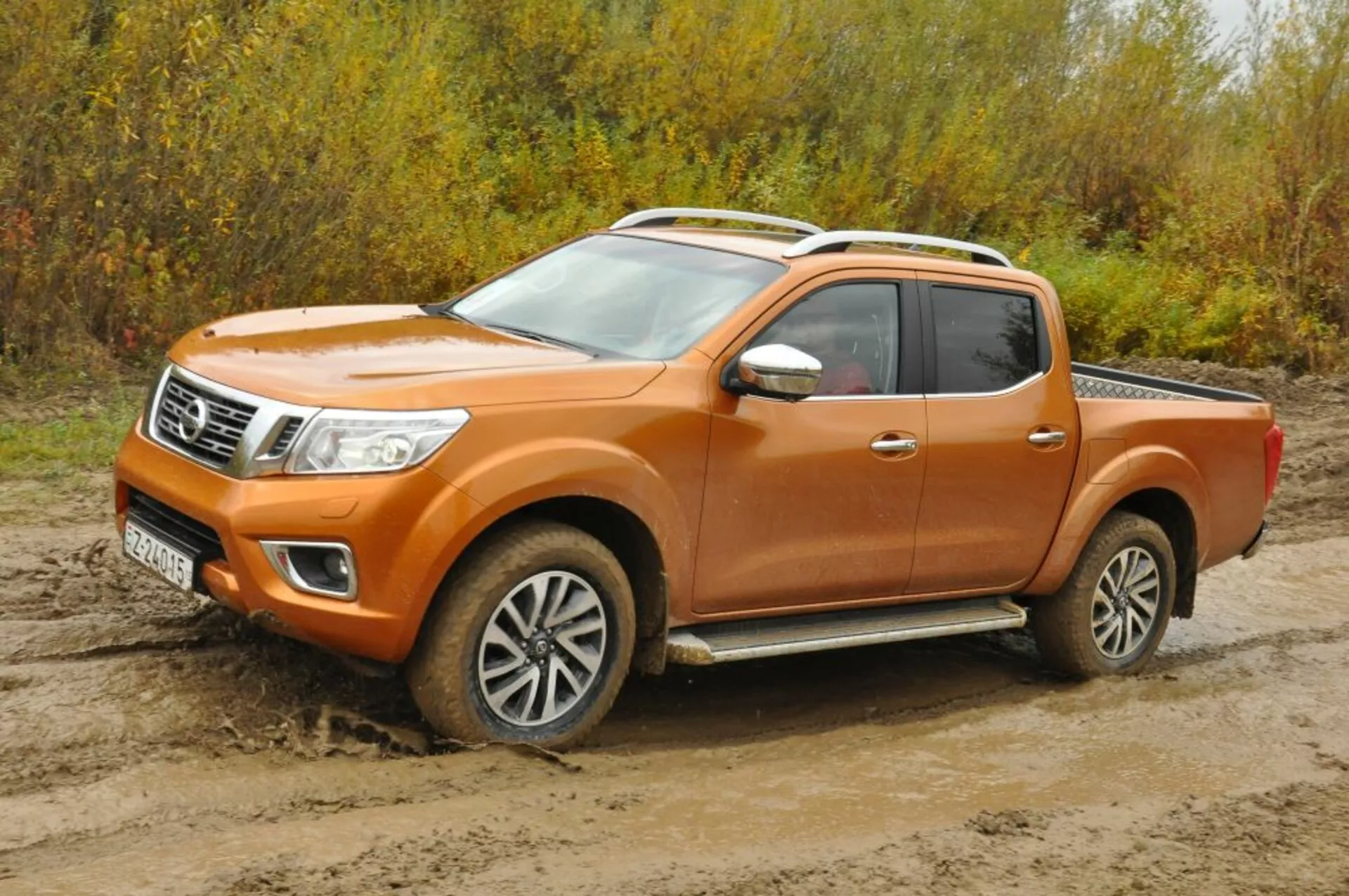 Camionnette Nissan Navara orange de 2016 vue de trois quarts avant, présentant phares, calandre accentuée de chrome, roues en alliage et configuration de la cabine d'équipage sur terrain accidenté