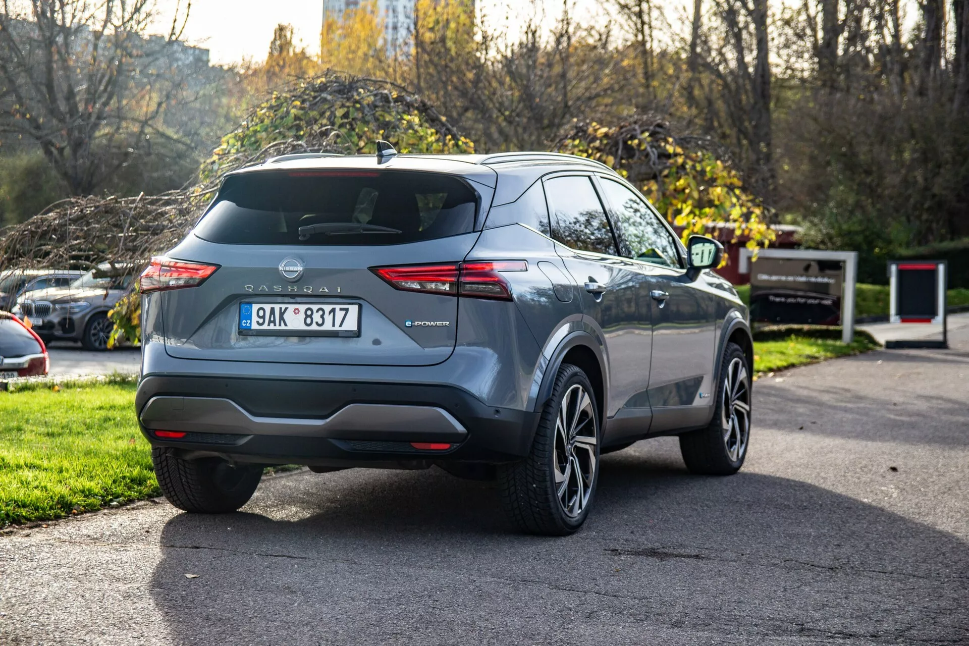 Véhicule Nissan Qashqai 2021 capturé sous un angle arrière trois-quarts, montrant des groupes optiques arrière distincts, hayon visible avec essuie-glace, badge du constructeur centré, plaque d'immatriculation montée, réflecteurs intégrés dans le pare-chocs arrière, embout d'échappement unique, roues en alliage, lignes de carrosserie modernes, fenêtres latérales effilées, éventuels rails de toit, antenne de toit courte, finition de peinture métallique et rétroviseur latéral partiellement visible.