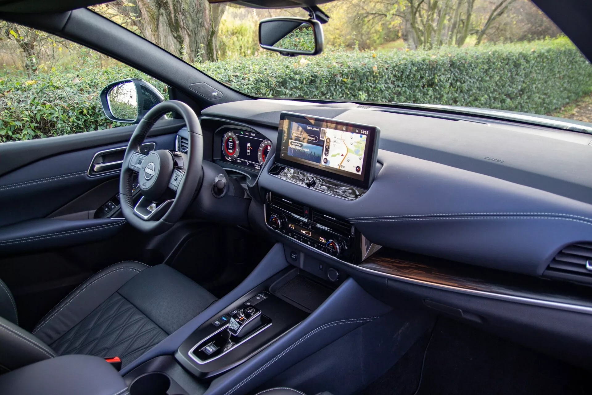 Vue intérieure de la Nissan Qashqai 2021 depuis la perspective du siège arrière, présentant la cabine avant moderne avec un volant multifonction, un tableau de bord entièrement numérique et un grand écran tactile d'infodivertissement. La console centrale comprend un levier de vitesse automatique, des boutons de contrôle du climat et des options de connectivité, avec des sièges avant en cuir et des matériaux haut de gamme sur le tableau de bord et la console.