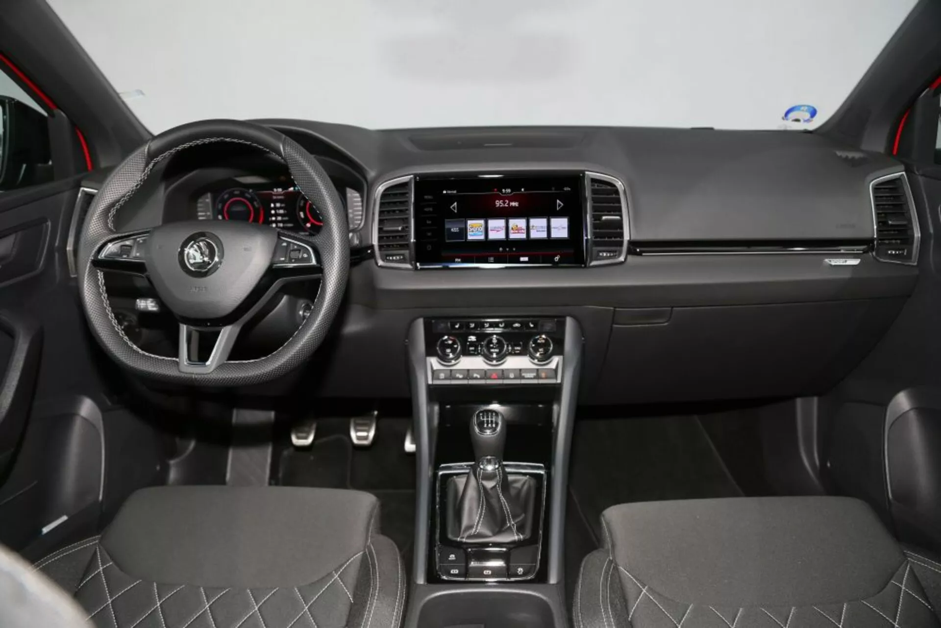 Vue intérieure du Nissan Qashqai 2014 montrant le volant avec commandes multifonctions, le cluster d'instruments derrière, grand écran d'infodivertissement sur le tableau de bord, système de contrôle climatique, levier de vitesse manuelle, sièges avant avec design en motif de diamant et caractéristiques de voiture moderne