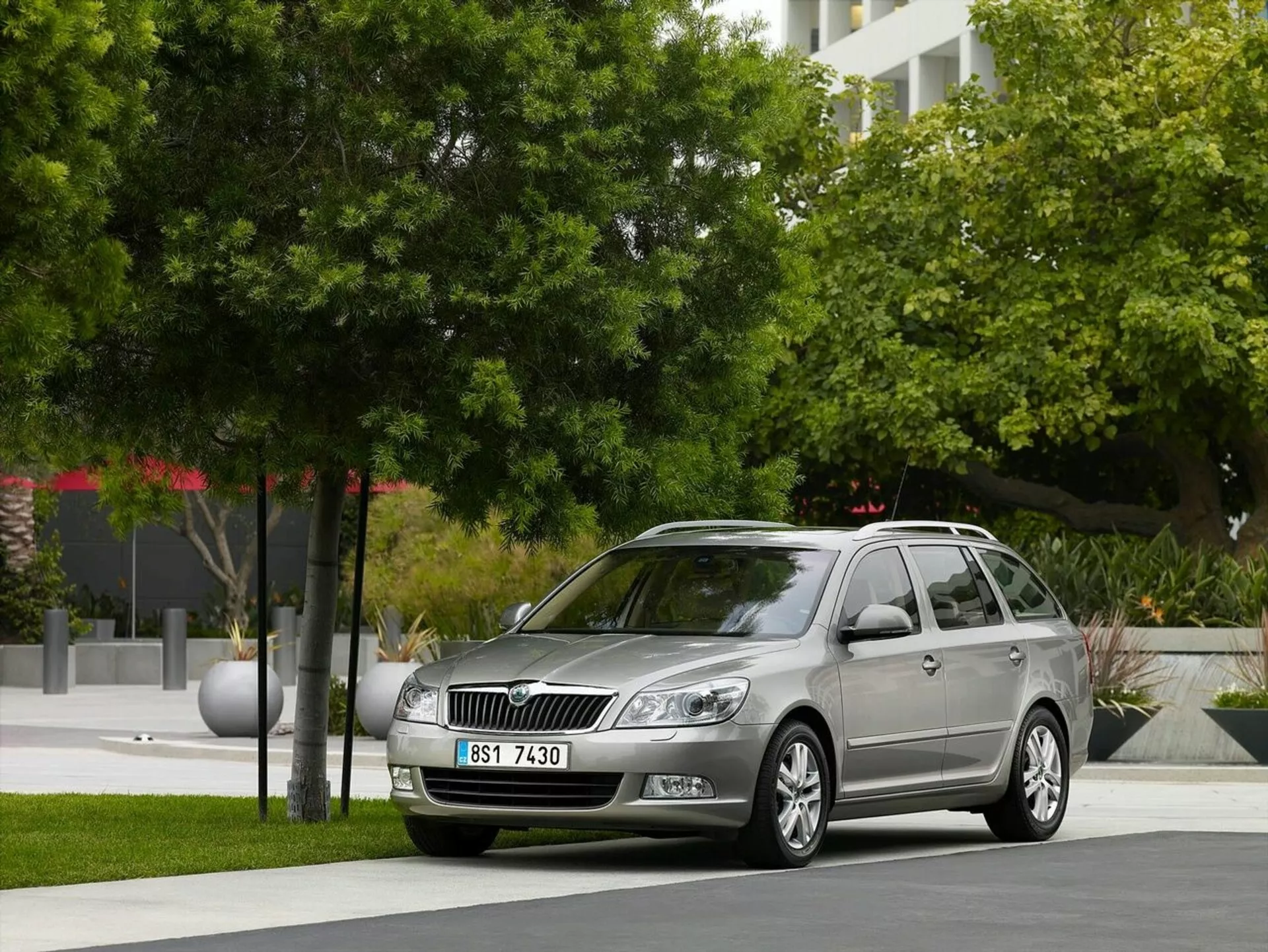 Station wagon Opel Astra de 2011 garée dans un cadre urbain avec de la verdure et des bâtiments modernes en arrière-plan, mettant en avant la grille avant de la voiture, les phares et un profil latéral élégant incluant des roues en alliage et des barres de toit