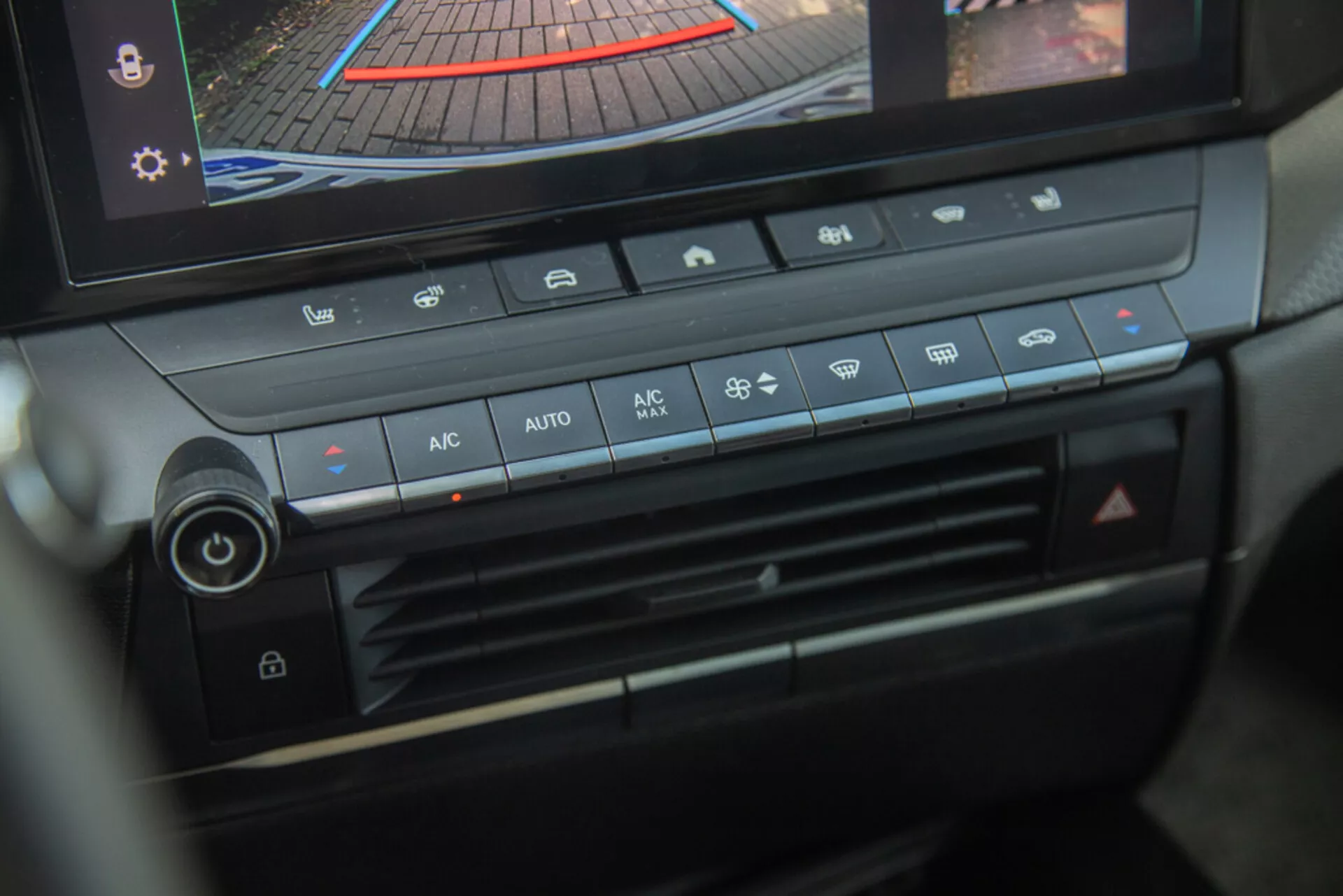 Console centrale et panneau de contrôle climatique de l'Opel Astra 2022, mettant en avant le bouton de réglage de la température, la vitesse du ventilateur, la distribution de l'air et les boutons du contrôle climatique automatique avec affichage numérique montrant la caméra de recul