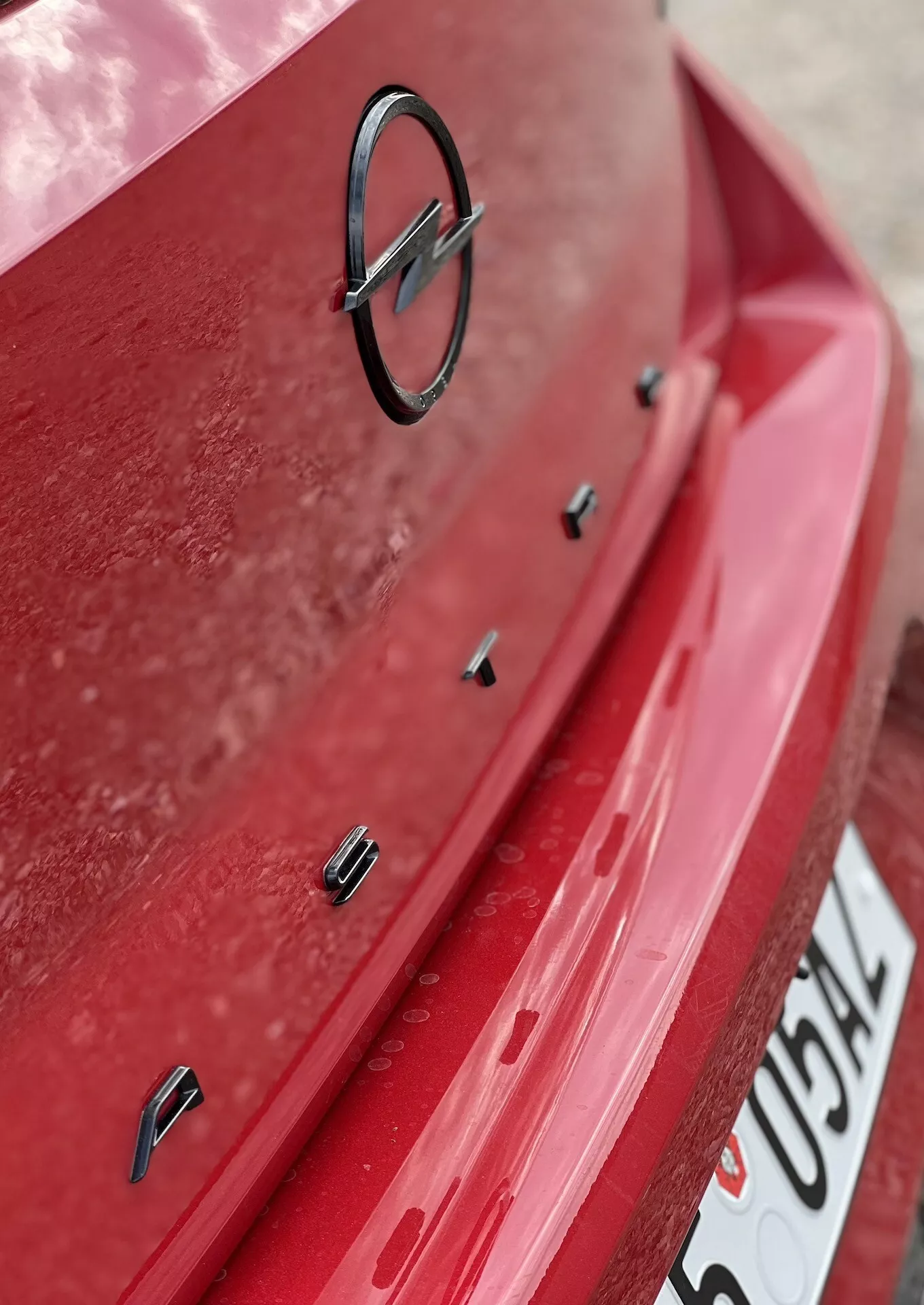 Vue rapprochée de la section arrière de l'Opel Astra 2022 avec peinture rouge et couche de poussière visible, affichant l'emblème du fabricant et des capteurs d'aide au stationnement