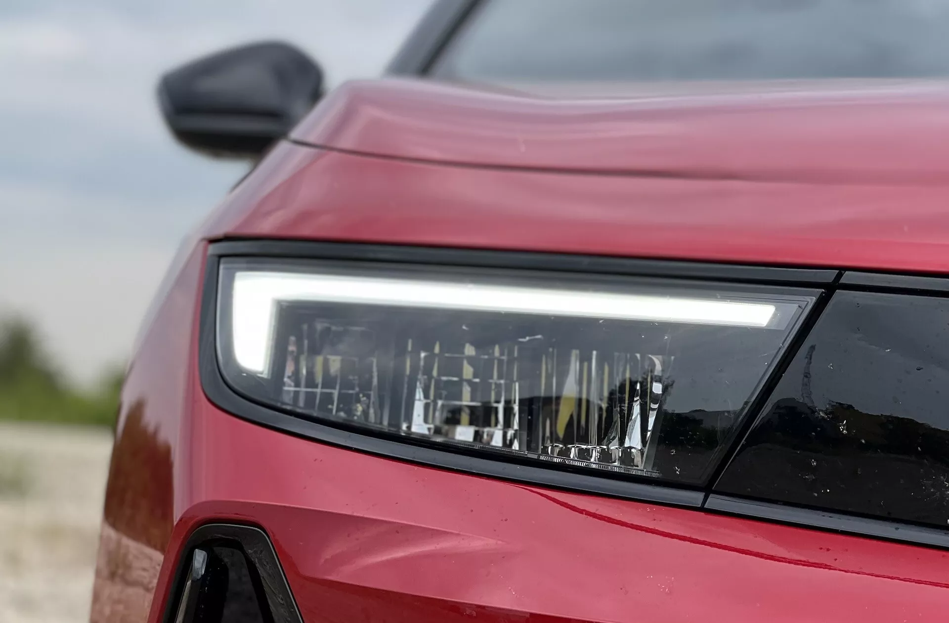 Vue rapprochée et latérale avant d'une Opel Astra rouge 2022 focalisée sur la conception détaillée du phare LED, mettant en avant la technologie d'éclairage moderne et les contours du véhicule