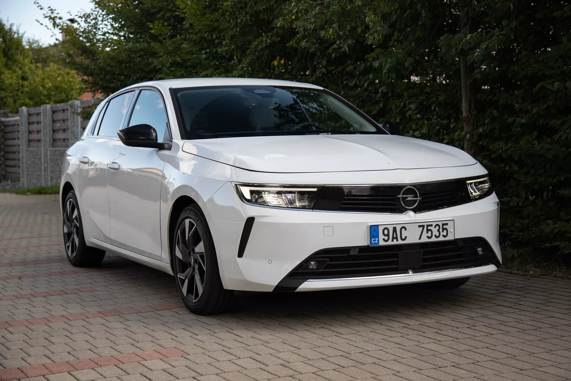 Opel Astra 2022 capturée dans un cadre suburbain, présentant ses phares élégants, sa grille avant proéminente, son design aérodynamique incluant des roues en alliage à multiples branches, et sa technologie innovante sous un angle de vue frontal de trois quarts