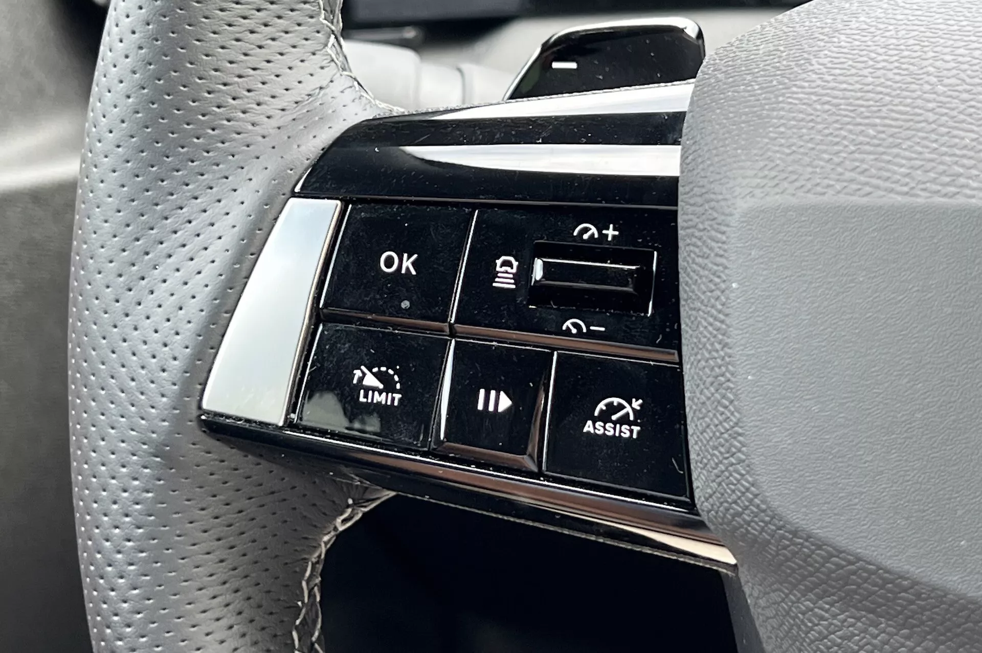 Gros plan sur le cluster de boutons du volant de l'Opel Astra 2022 mettant en évidence les fonctionnalités avancées d'aide à la conduite, y compris le régulateur de vitesse adaptatif et l'assistance au maintien de voie, avec une concentration sur les étiquettes fonctionnelles telles que OK, +, -, LIMIT et ASSIST du point de vue du conducteur