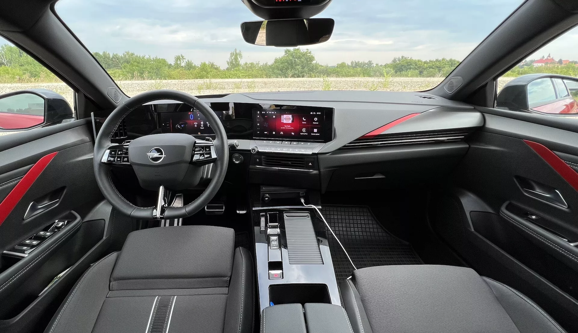 Intérieur de l'Opel Astra 2022 présentant un volant multifonction à trois branches, un tableau de bord numérique, un système d'infodivertissement tactile, des commandes de climatisation épurées, des finitions en cuir bicolore à coutures rouges, et un design moderne de l'habitacle vu depuis le poste de conduite