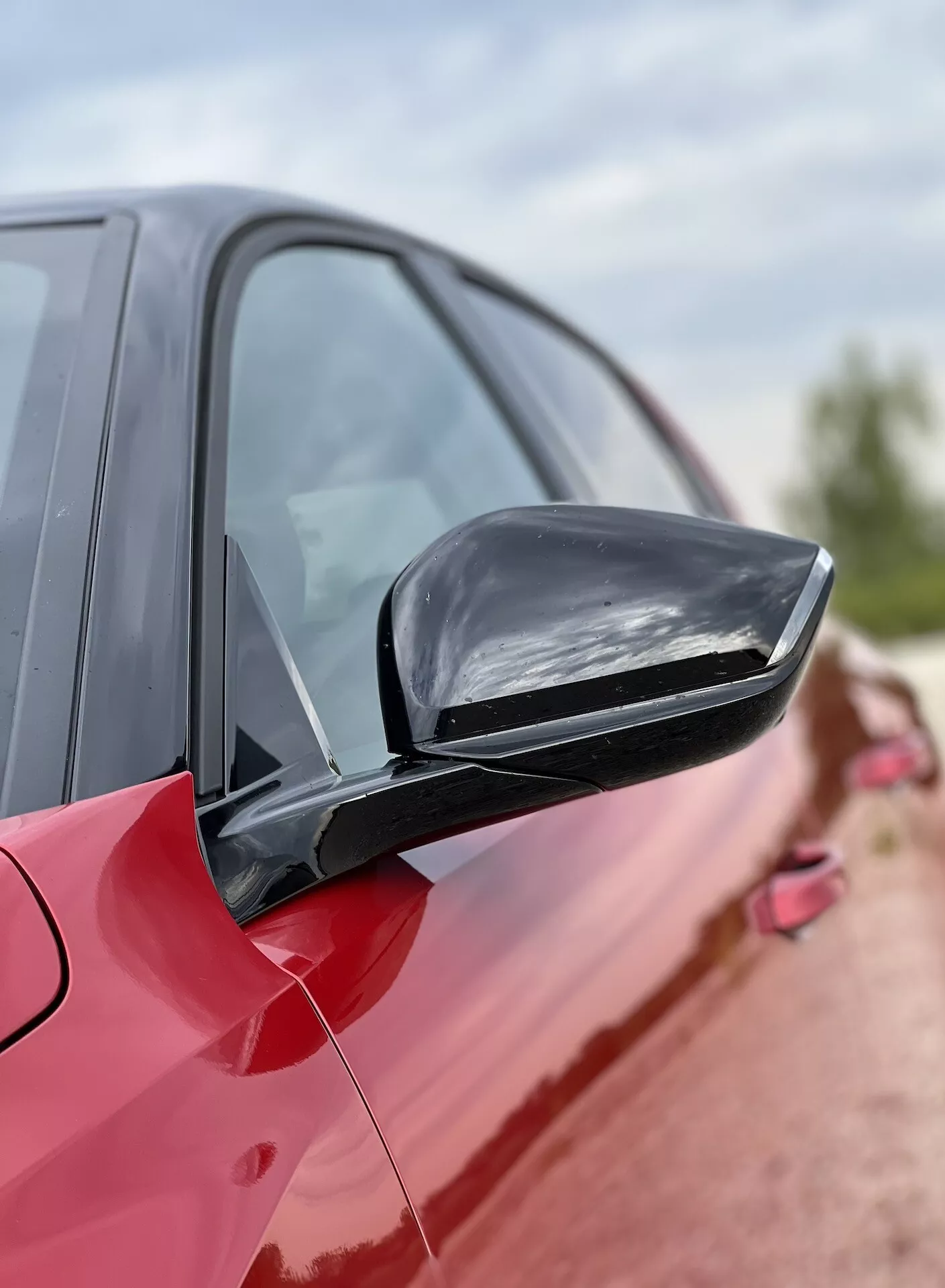 Gros plan sur un rétroviseur latéral d'une Opel Astra 2022 en rouge, mettant en avant le design élégant et assorti à la couleur et les éventuelles fonctionnalités technologiques sur fond de silhouette floue de la voiture
