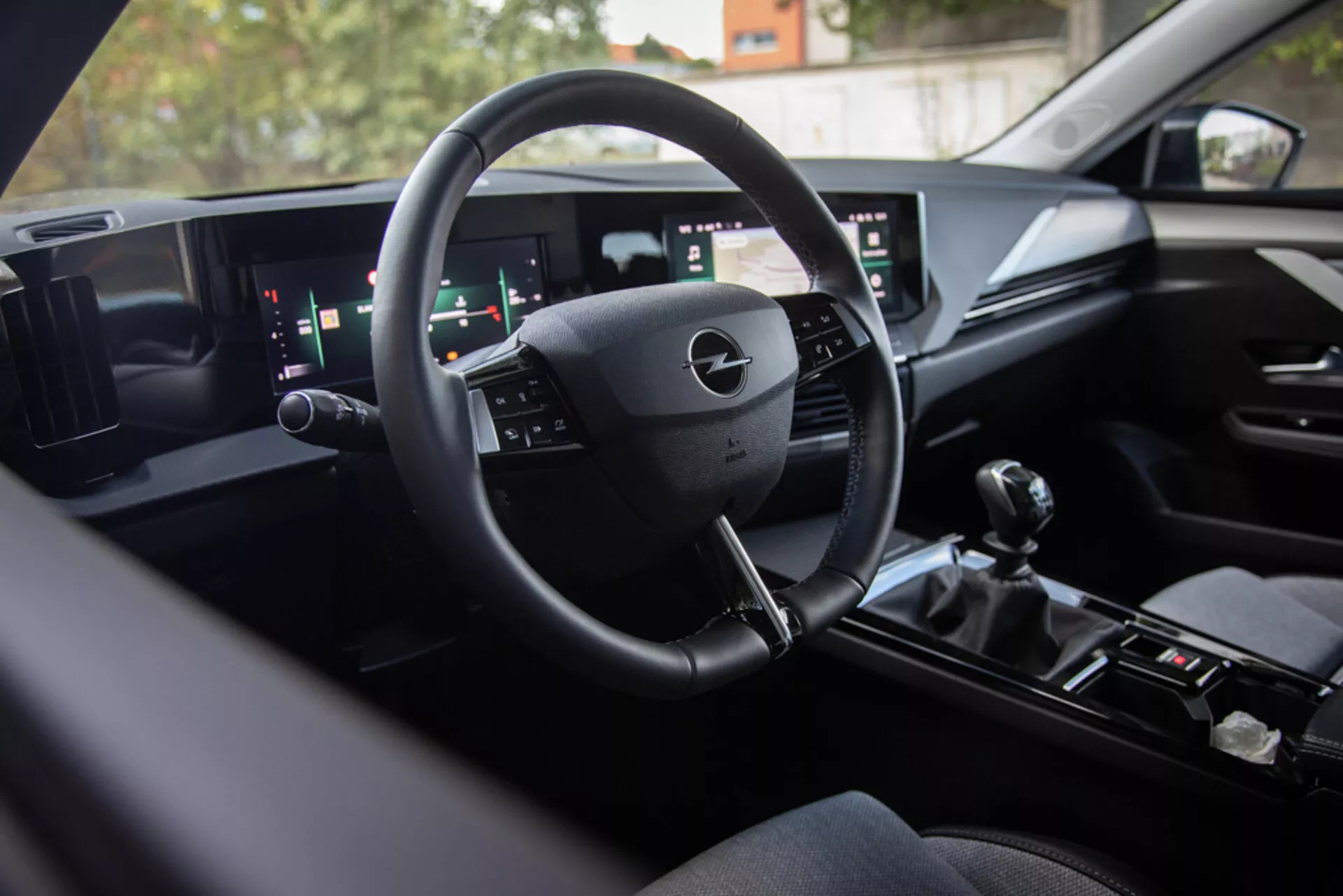 Intérieur de l'Opel Astra 2022 exposant une technologie de tableau de bord digital moderne, volant multifonctions, système d'infodivertissement à écran large double et levier de vitesse manuel pour des performances sportives, vue de l'arrière vers la zone du conducteur avec des finitions premium