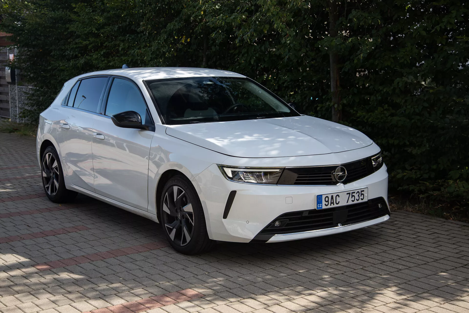 Opel Astra 2022 blanche avec façade avant distincte, phares élancés, grille horizontale, pare-chocs aérodynamique, capot profilé et jantes en alliage à multiples branches capturée sous un angle avant trois quarts à l'extérieur en journée