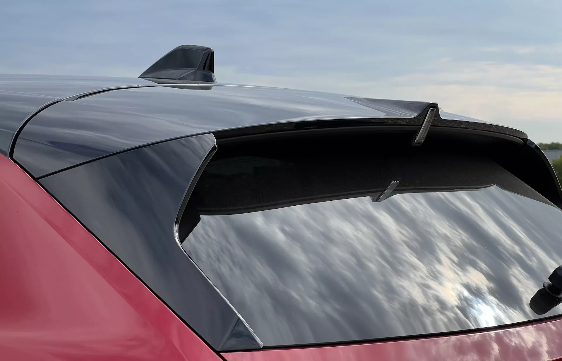 Vue rapprochée de la section arrière rouge brillant d'une Opel Astra 2022 avec un spoiler élégant et une antenne aileron de requin, soulignant le grand pare-brise arrière aérodynamique avec potentiel teinté de protection UV.