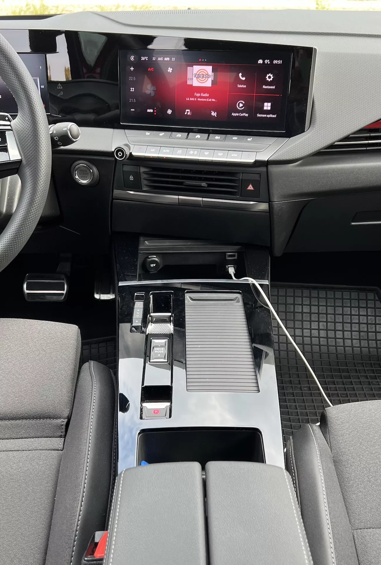 Vue intérieure de l'Opel Astra 2022 montrant la conception moderne de la cabine avec système d'infodivertissement tactile, commandes de climatisation sensibles au toucher, levier de vitesses métallique, connectivité USB, porte-gobelets, accoudoir central détaillé, sièges bicolores et détails de la cabine en matériaux mixtes avec tapis de sol durables