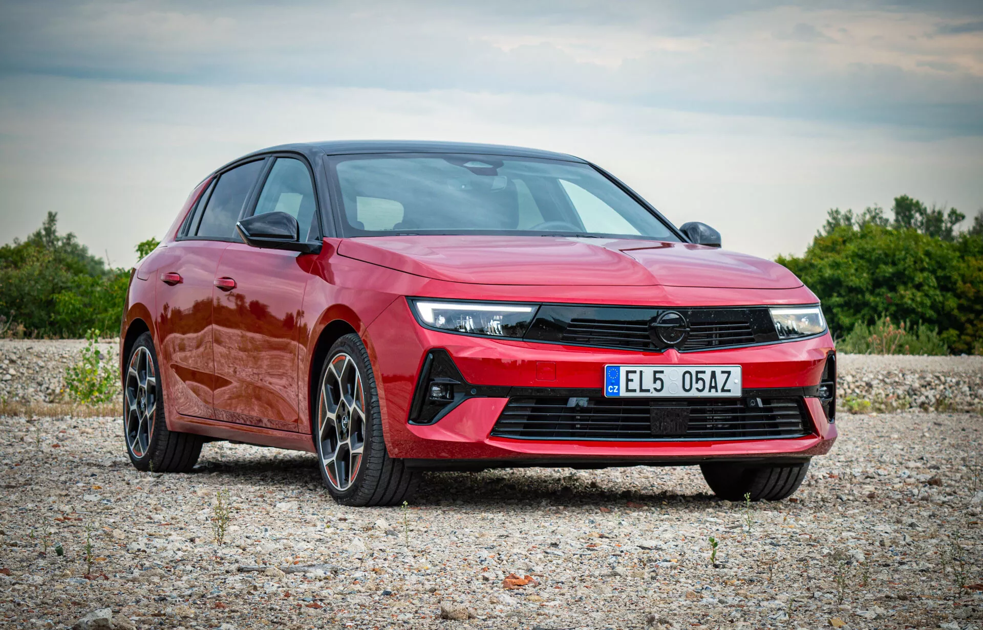 Opel Astra 2022 en rouge vif, affichant un design moderne avec des phares LED angulaires, une grille avant proéminente, un pare-chocs avant sportif et des jantes en alliage à plusieurs branches, présentée dans un cadre naturel en extérieur depuis une vue de trois quarts avant mettant en lumière le profil aérodynamique et les caractéristiques haut de gamme de la voiture