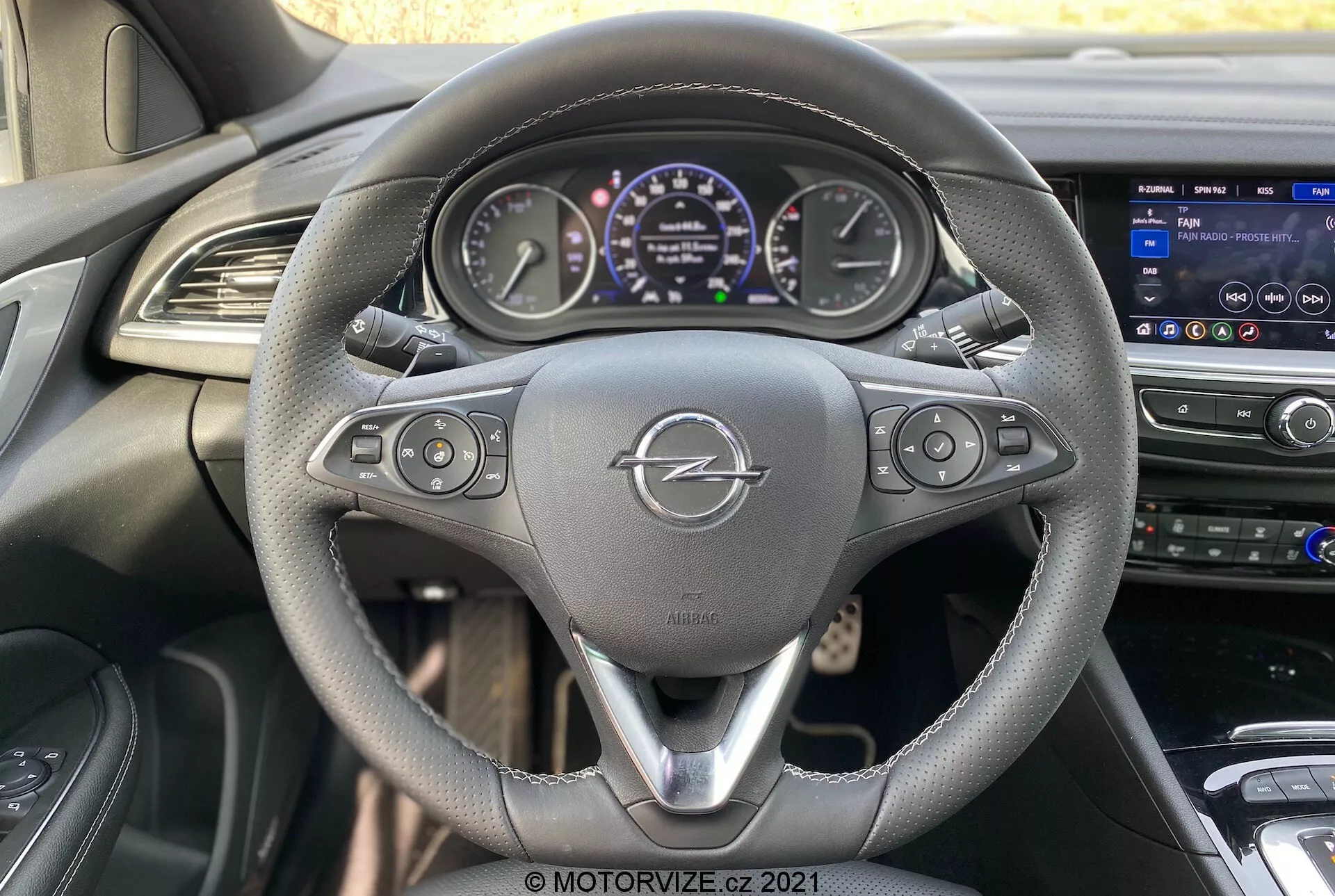 Vue intérieure de l'Opel Insignia GSi Grand Sport 2020 depuis le siège du conducteur, avec un volant en cuir à trois branches équipé de boutons de commande, un tableau de bord numérique affichant des jauges et des informations sur le véhicule, et une console centrale avec un système d'infodivertissement à écran tactile et des bouches d'aération pour le contrôle du climat.