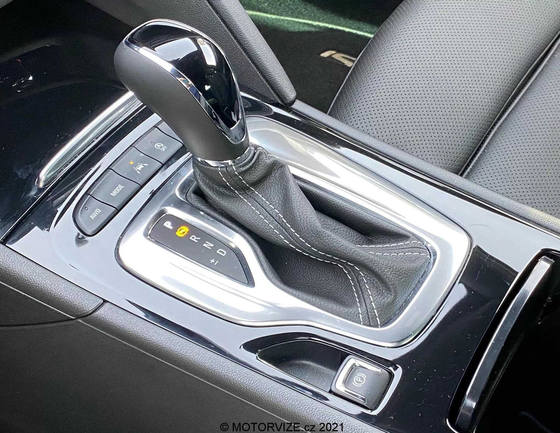Vue rapprochée du levier de vitesses automatique de l'Opel Insignia GSi Grand Sport 2020, mettant en évidence la console centrale élégante vue de haut. Le levier de vitesses, avec sa finition métallique, est en position 'P', entouré d'une console noire brillante avec des accents argentés. Les boutons visibles et les indicateurs lumineux suggèrent des contrôles électroniques modernes et des modes de conduite.