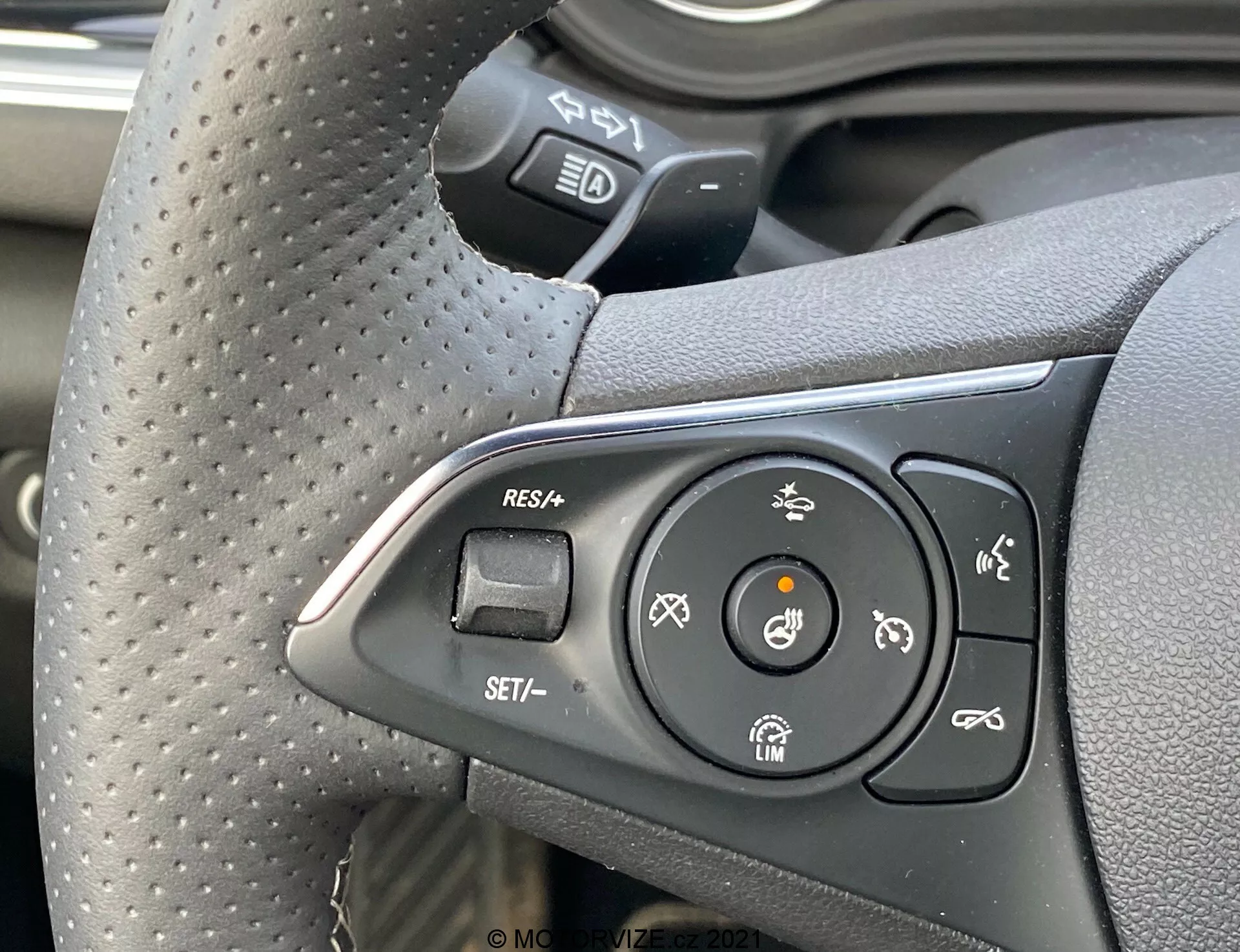Vue rapprochée du groupe de contrôle situé à gauche du volant d'une Opel Insignia GSi Grand Sport 2020 depuis la perspective du conducteur, montrant les boutons du régulateur de vitesse, du volant chauffant et de l'assistance au maintien de voie, avec une prise texturée indiquant confort et sportivité.