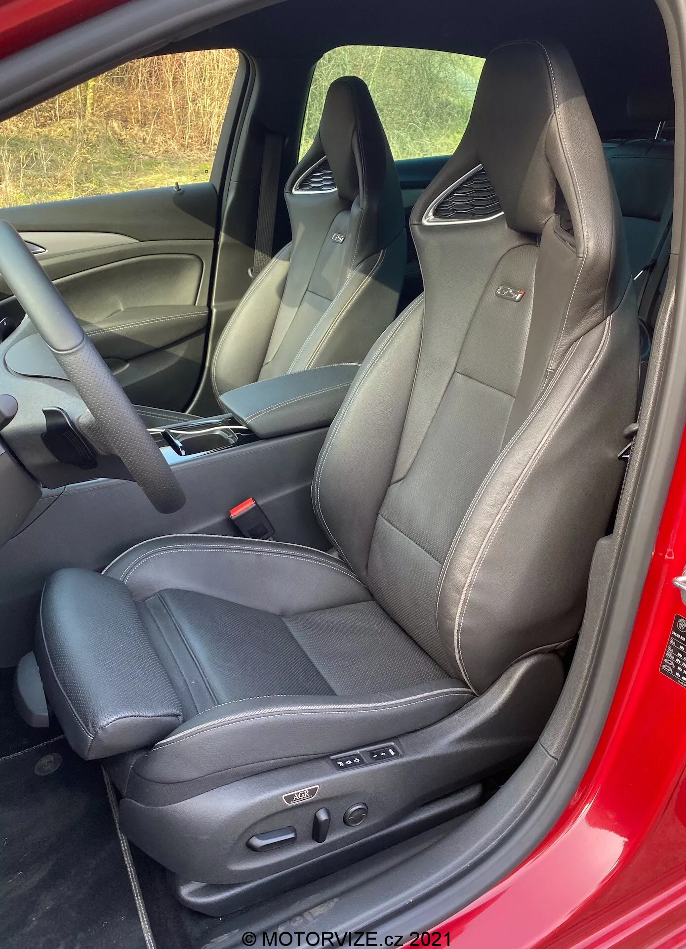 Vue intérieure en gros plan de l'Opel Insignia GSi Grand Sport 2020 avec siège conducteur sportif de luxe en cuir noir avec coutures apparentes, prise d'un angle légèrement surélevé et diagonal, avec appui-tête intégré, panneau de commande électronique, panneau de porte et tableau de bord partiellement visibles.