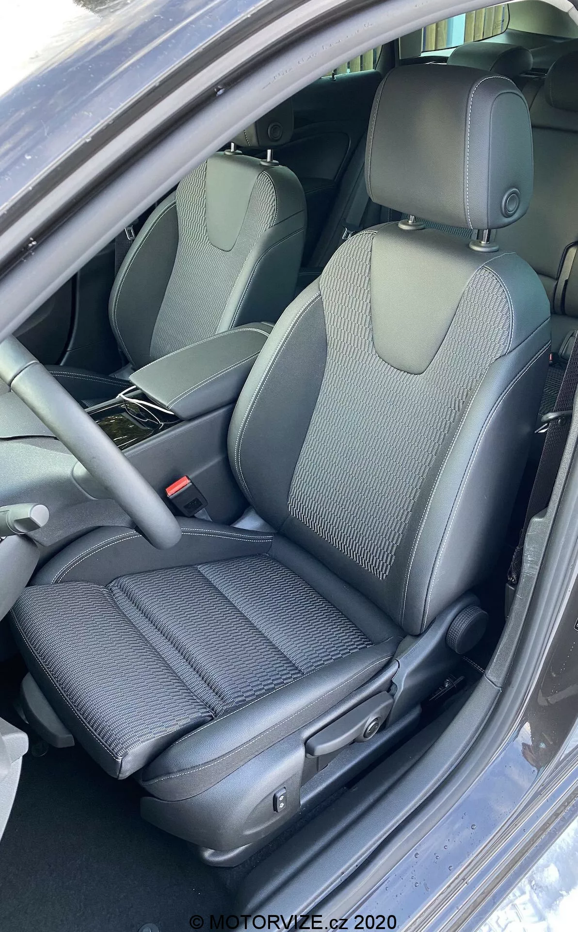 Vue rapprochée, prise verticale de l'intérieur de la voiture Opel Insignia 2020 (Insignia Sports Tourer) centrée sur le siège conducteur avant avec un design mixte en tissu et cuir synthétique, commandes de réglage manuel du siège, volant multifonction partiellement visible et ceintures de sécurité réglables en hauteur, mettant en avant les caractéristiques ergonomiques et de rembourrage.