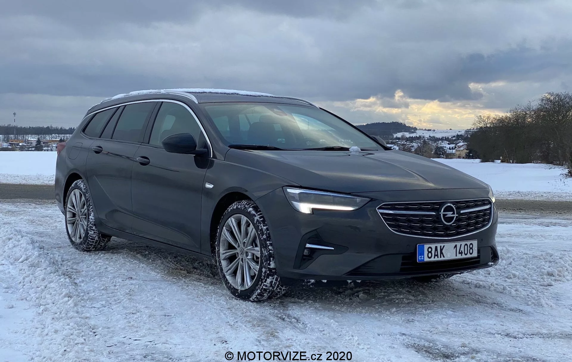 Image d'une voiture Opel Insignia Sports Tourer 2020 moderne dans un décor hivernal enneigé, ciel nuageux en arrière-plan, montrant sa calandre avant, ses phares LED élégants, son capot sculpté, son système de rails de toit, ses fenêtres latérales encadrées de chrome, ses roues en alliage à plusieurs branches avec pneus hiver et état général de la route en hiver.