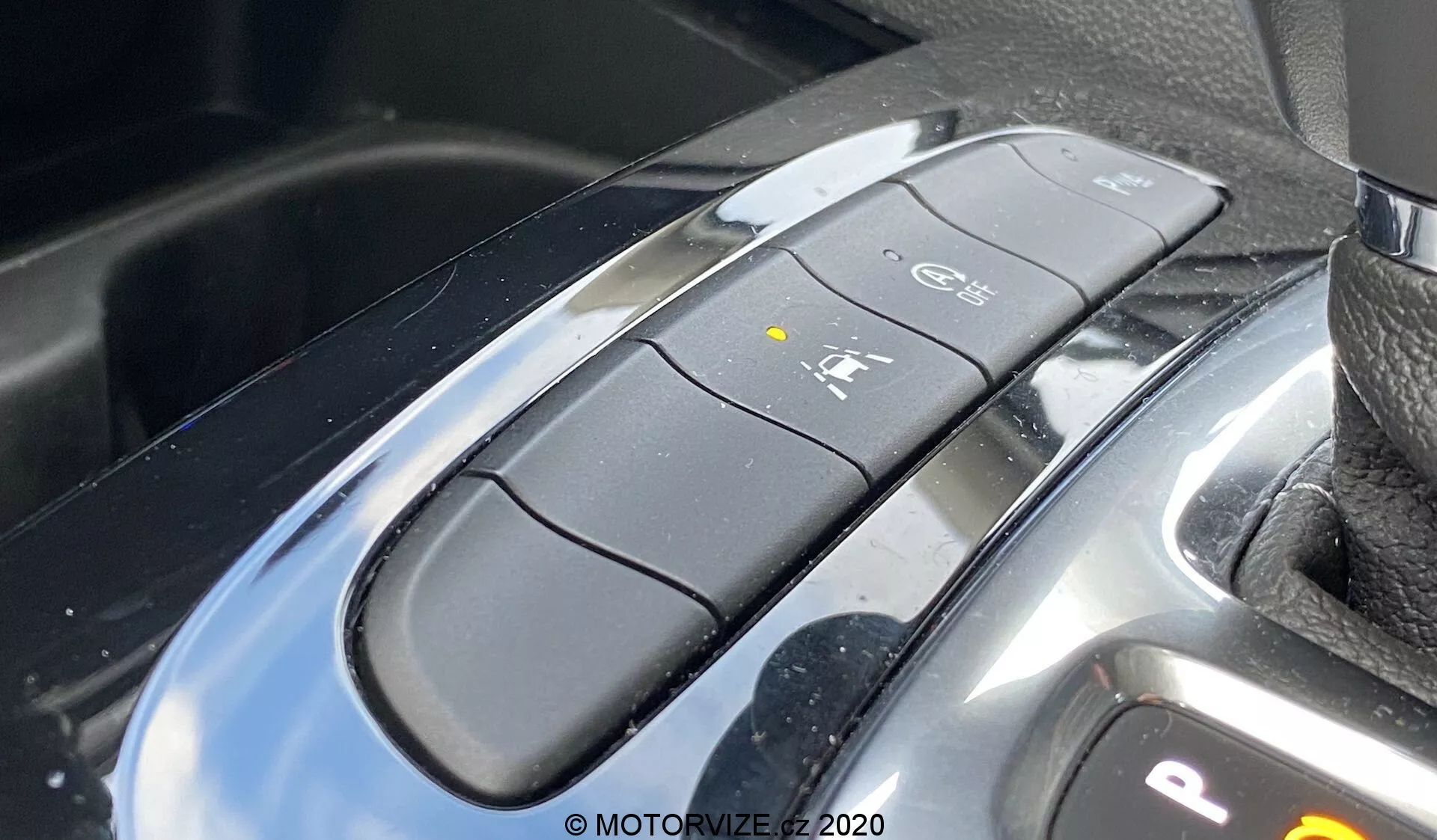 Gros plan de l'intérieur de l'Opel Insignia 2020 Sports Tourer, axé sur la zone de la console centrale. Présente en évidence le sélecteur de vitesse moderne avec finition noire brillante et accents argentés. Boutons multi-fonctions incluant 'Park' ('P'), 'Reverse' ('R'), 'Drive' ('D'), système auto stop/start ('A') et verrouillage de stationnement ou frein de stationnement électronique. Surface métallique réfléchissante de la console, indiquant un design haut de gamme.