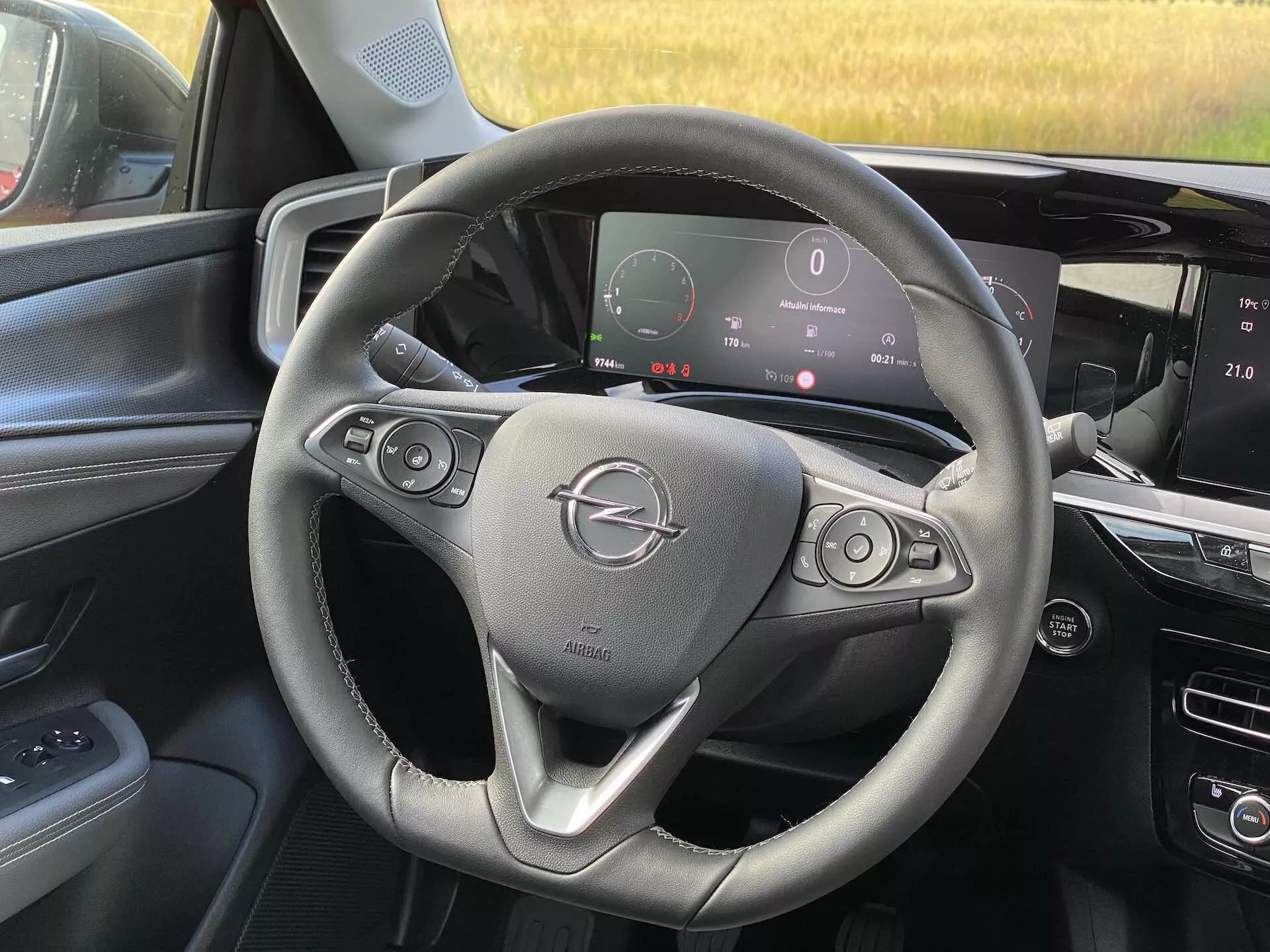 Vue intérieure de l'Opel Mokka 2021 depuis la perspective du siège passager avant, montrant le volant avec des boutons de contrôle audio et de régulateur de vitesse, le tableau de bord numérique affichant le tachymètre et d'autres métriques, et la console centrale avec un système d'infodivertissement à écran tactile.