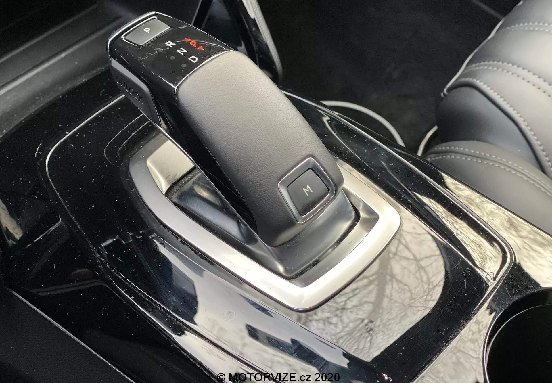 Gros plan de la perspective latérale intérieure du Peugeot 2008 2020 avec un élégant levier de vitesses, présentant une transmission automatique avec étiquettes 'P', 'R', 'N', 'D' et 'M' pour le mode manuel, sur une console centrale noire brillante avec des accents chromés et des alentours en apparence cuir, indicatif d'un intérieur de voiture premium.