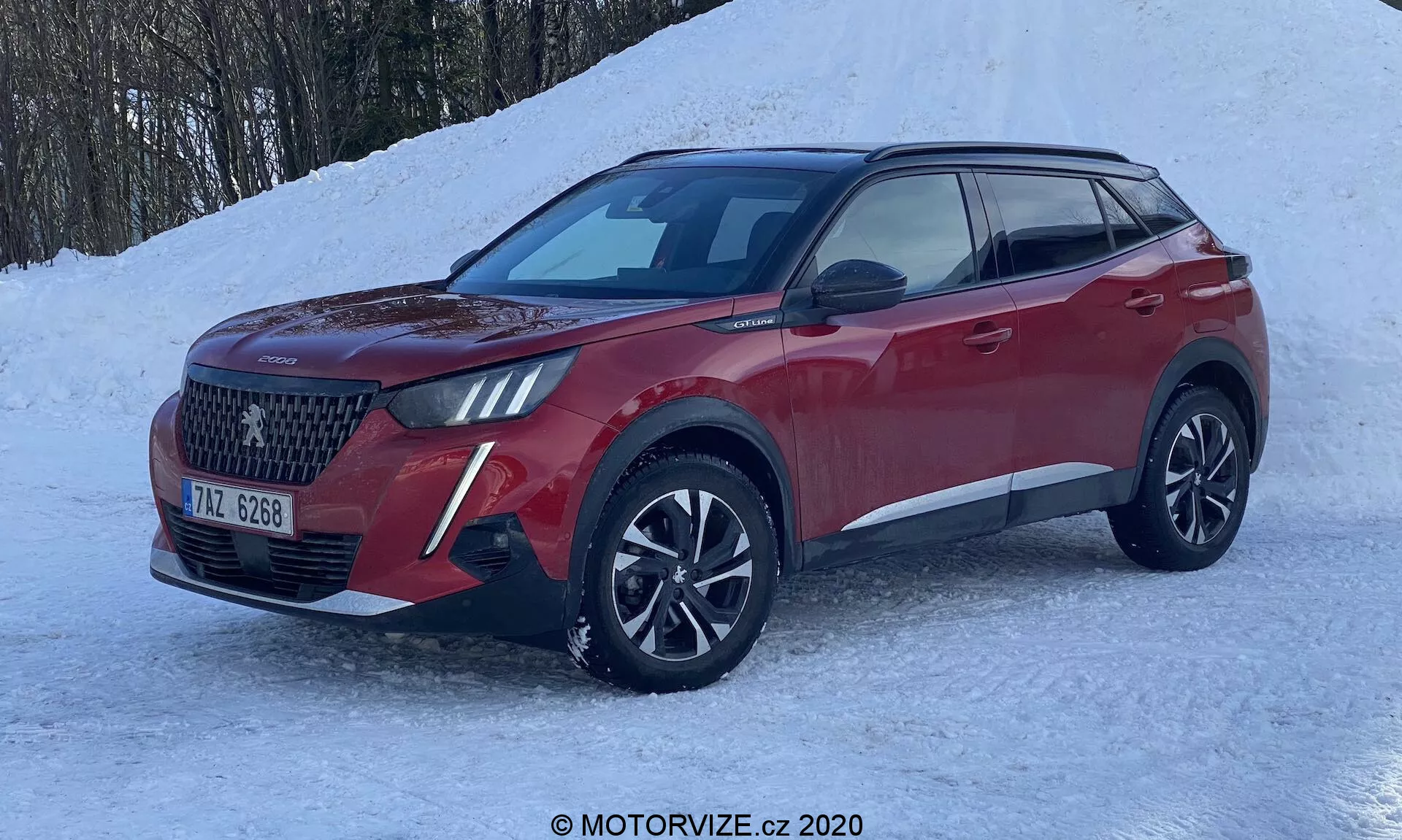 SUV moderne Peugeot 2008 1.2 PureTech 100 Active 2020 en vue avant trois quarts, mettant en évidence une grande calandre à motif en diamant, des phares à LED avec feux de jour, des roues en alliage multi-rayons et une carrosserie sculptée rouge métallique. Positionné sur un sol enneigé, suggérant des capacités de conduite hivernale telle que la traction intégrale.