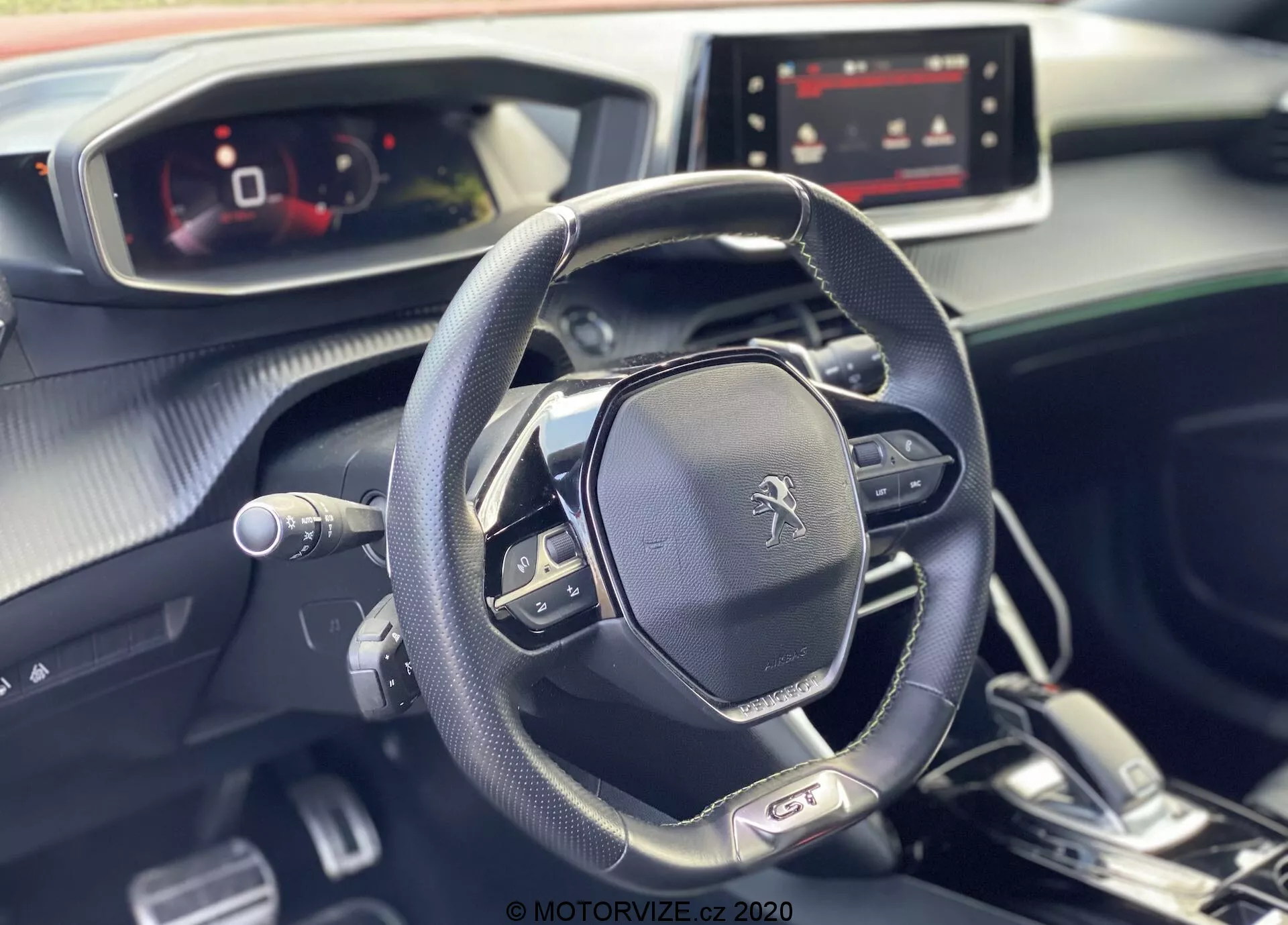 L'image met en avant l'intérieur moderne et élégant de la Peugeot 2008 2020, en se concentrant sur le volant multifonction et le tableau de bord entièrement numérique depuis la perspective du côté passager. Le logo Peugeot est bien en évidence sur le volant, qui comporte des commandes multimédias, des réglages de régulateur de vitesse et des palettes, suggérant une transmission automatique avec des options de changement de vitesse manuel. Le tableau de bord, conçu avec un mélange de matériaux doux au toucher et d'accent métalliques, inclut un écran d'infodivertissement allumé, indiquant diverses options de connectivité et de navigation. La lumière naturelle améliore l'atmosphère impeccable et accueillante de l'intérieur de la voiture.