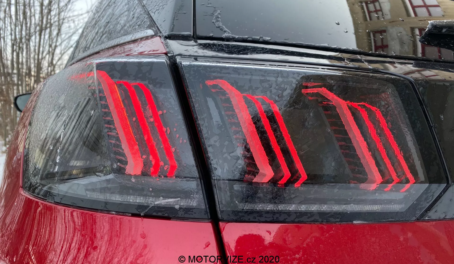 Gros plan sur la partie arrière d'une Peugeot 3008 de 2021, mettant en avant le design moderne des feux arrière à LED verticalement illuminés sur une carrosserie rouge brillante avec des gouttelettes d'eau, suggérant un cadre extérieur pendant ou après la pluie; les feux arrière sont dotés d'une technologie économe en énergie et servent d'indicateurs de feux de freinage et de fonctionnement.