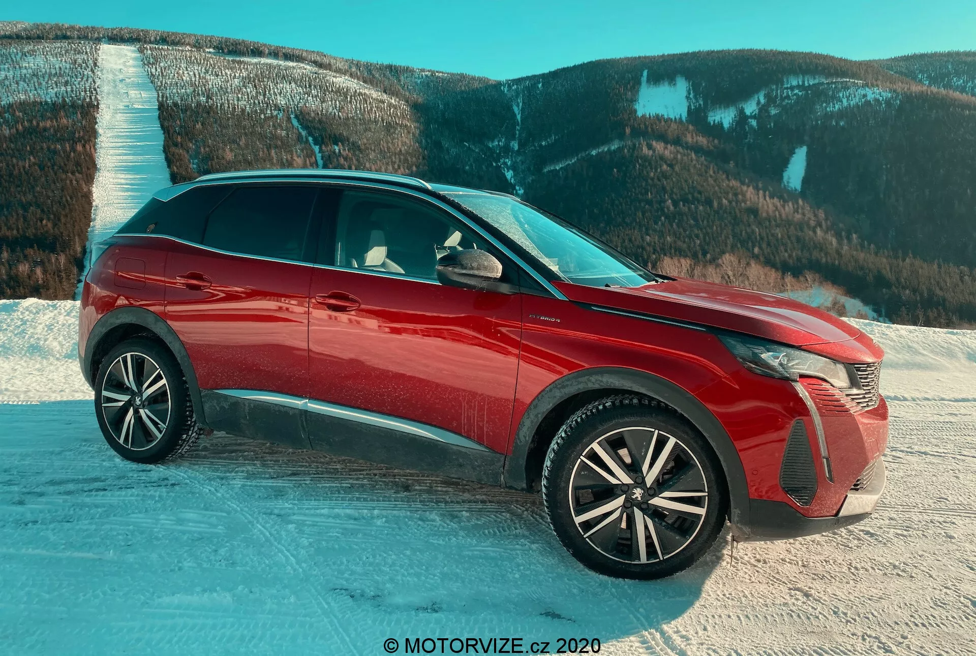 SUV Peugeot 3008 2021 rouge, capturé en vue de trois quarts avant sur une surface enneigée avec un arrière-plan montagnard, soulignant les phares LED avancés, les roues en alliage complexes, la finition brillante, les volets de calandre actifs et les rétroviseurs latéraux avec clignotants intégrés, mettant en avant les éléments de design et la pertinence pour des conditions difficiles.