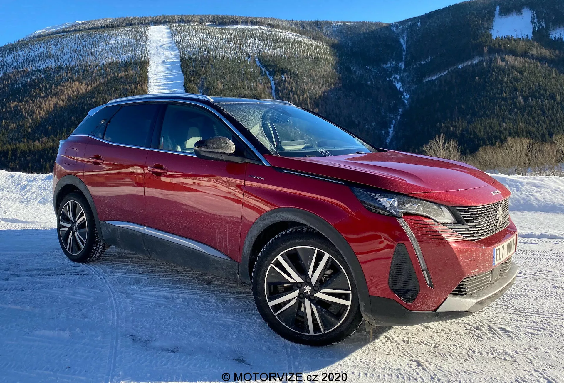 Image d'une voiture moderne, probablement une Peugeot 3008 de 2021, prise sous un angle de trois quarts avant. L'angle met en valeur le design distinct des phares à LED de la voiture, la grille en forme de peigne et l'emblème à l'avant. Le pare-chocs avant affiche des sections d'admission d'air et des logements de phares antibrouillard. Le capot présente des lignes sculptées, contribuant à l'aérodynamisme, tandis que le pare-brise expansif indique une bonne visibilité vers l'avant. Les roues en alliage multi-branches suggèrent un niveau de finition plus sportif et supérieur. La ligne de toit élégante et les lignes dynamiques de la carrosserie laissent entendre un crossover ou un SUV. Les rétroviseurs latéraux avec clignotants intégrés et les moulures latérales ou accents visibles. Le cadre est une route enneigée avec un arrière-plan montagneux, ce qui implique une capacité à affronter divers terrains.