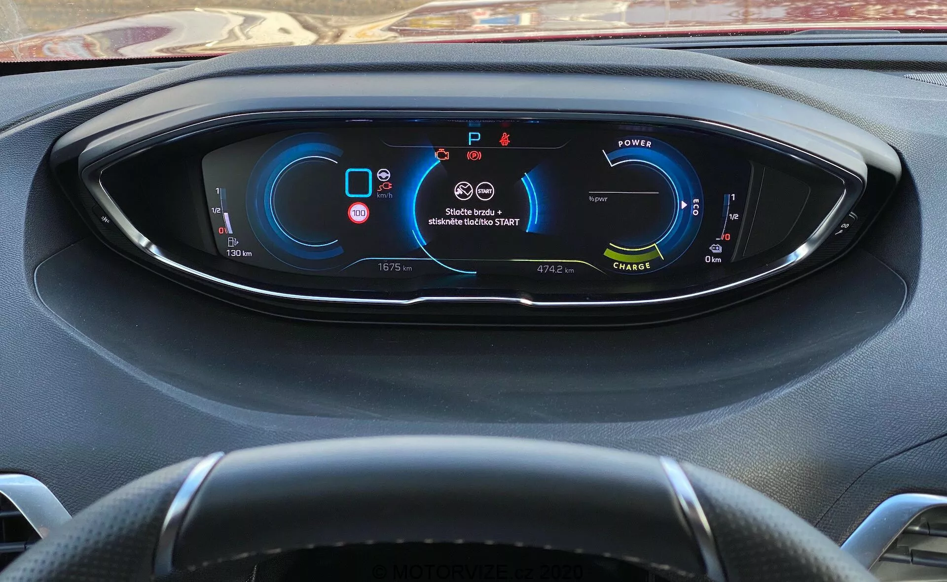 Vue du conducteur du tableau de bord du Peugeot 3008 de 2021 avec un tableau de bord entièrement numérique affichant les métriques et indicateurs du véhicule. À gauche, un indicateur de puissance suggère un véhicule électrique/hybride; au centre en haut, des avertissements de ceinture de sécurité et d'airbag; à droite, un compteur de vitesse indiquant que le véhicule est à l'arrêt; en bas, des informations sur le rapport (stationnement), l'odomètre, la température extérieure, les modes de conduite et l'autonomie disponible. Volant à trois branches partiellement visible. Vue de derrière le volant avec un léger angle vers le bas.