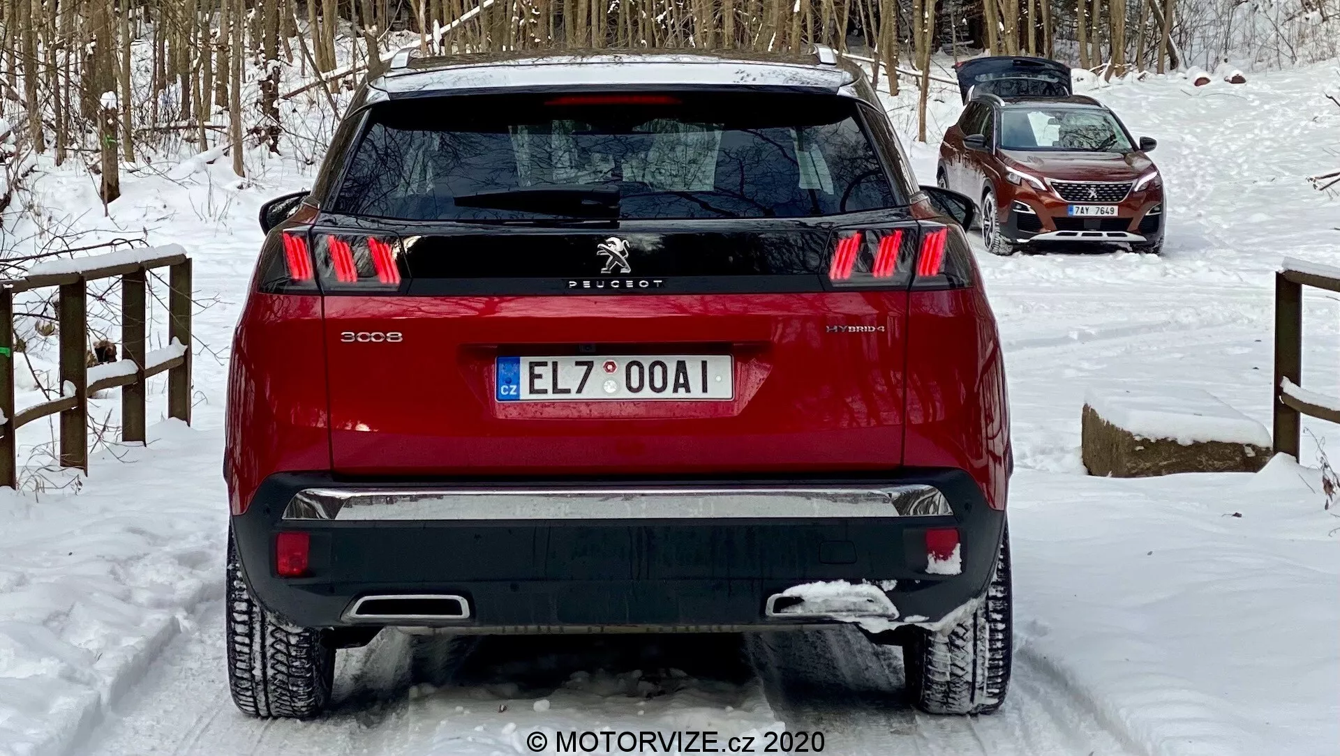 Vue arrière d'un SUV Peugeot 3008 rouge capturée sous un léger angle bas, mettant en avant ses feux arrière à trois griffes distinctives, l'emblème central du lion de Peugeot et le pare-chocs bi-ton. Le véhicule, positionné sur un sol enneigé, indique des conditions hivernales. Les caractéristiques visibles incluent des capteurs de stationnement arrière, un essuie-glace arrière et une antenne arrière supérieure, suggérant une technologie d'assistance au conducteur et une fonctionnalité potentielle GPS/radio, adaptée aux discussions sur la conception automobile, les caractéristiques de sécurité et la conduite hivernale.