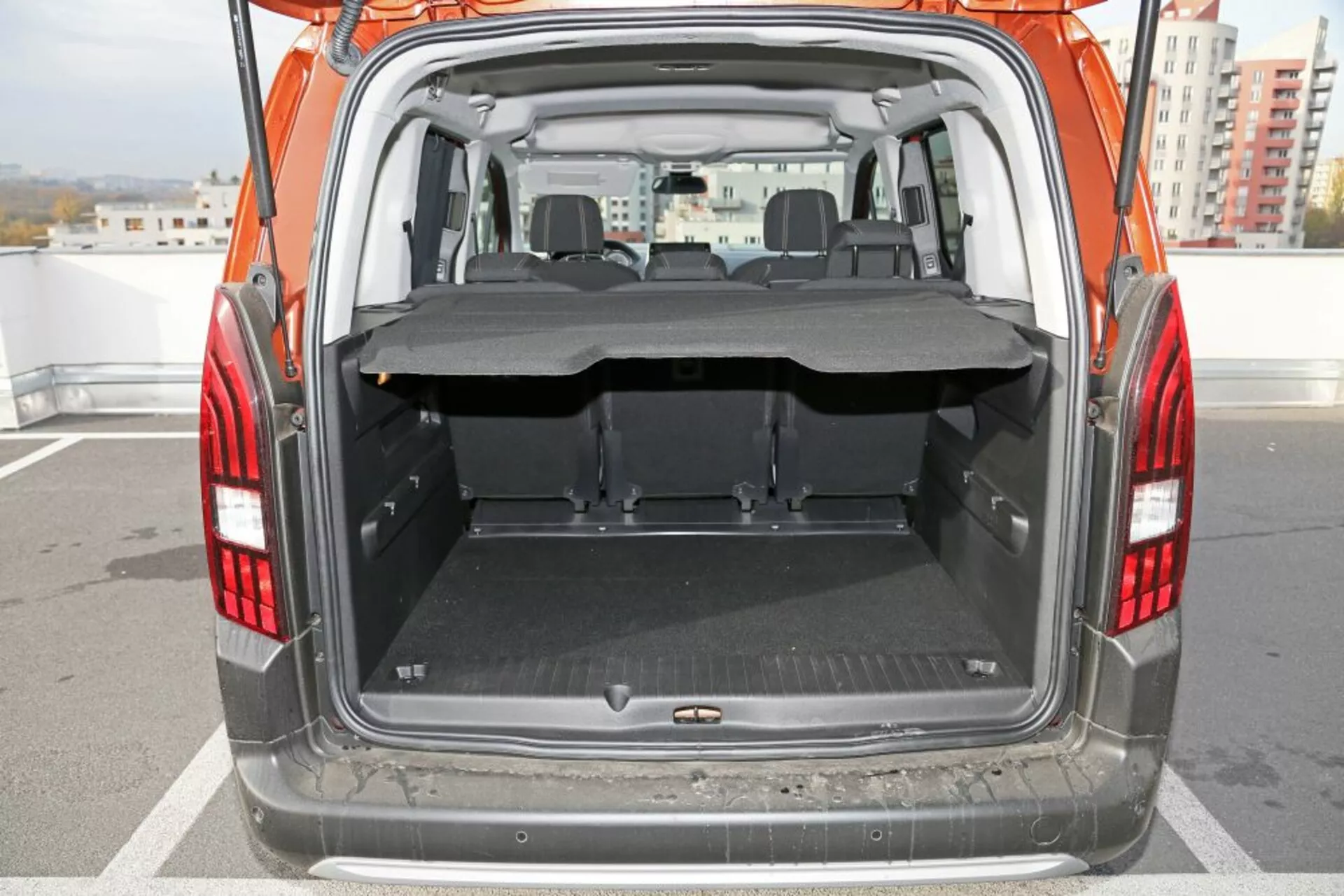 Vue de face du coffre ouvert d'une Peugeot 3008 de 2016 montrant un espace de chargement spacieux avec le siège arrière rabattu, un tapis protecteur et une couverture de chargement partiellement étendue en plein jour.