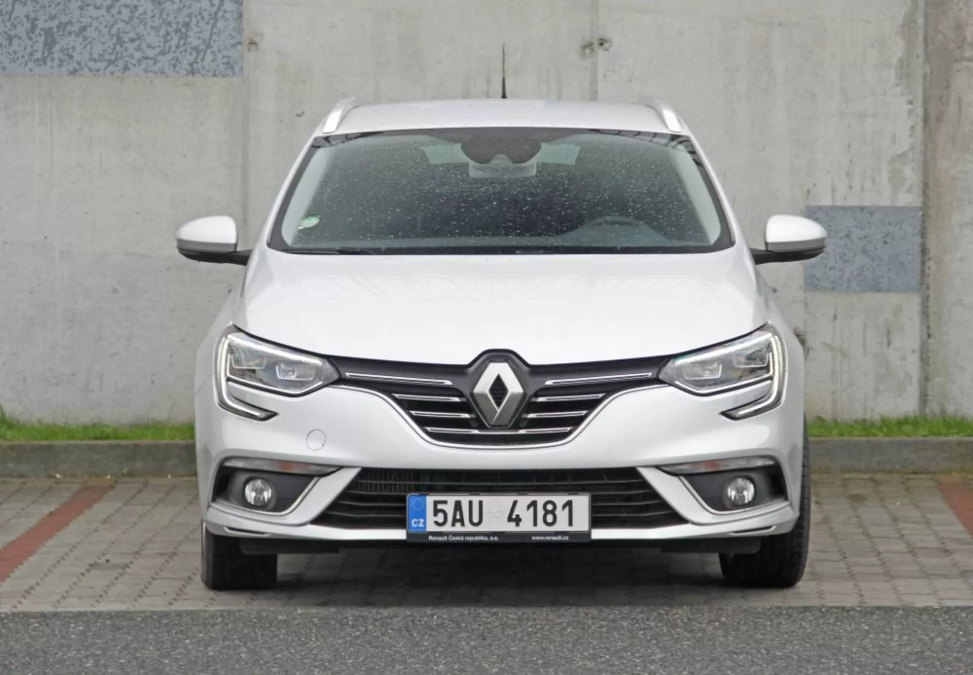 Vue de face directe d'une élégante Peugeot 308 SW 2013 blanche présentant une grille proéminente avec emblème Renault, des phares LED modernes avec feux de jour, des feux de brouillard intégrés et une technologie de capteur de stationnement, soulignant un design moderne et l'aérodynamisme.