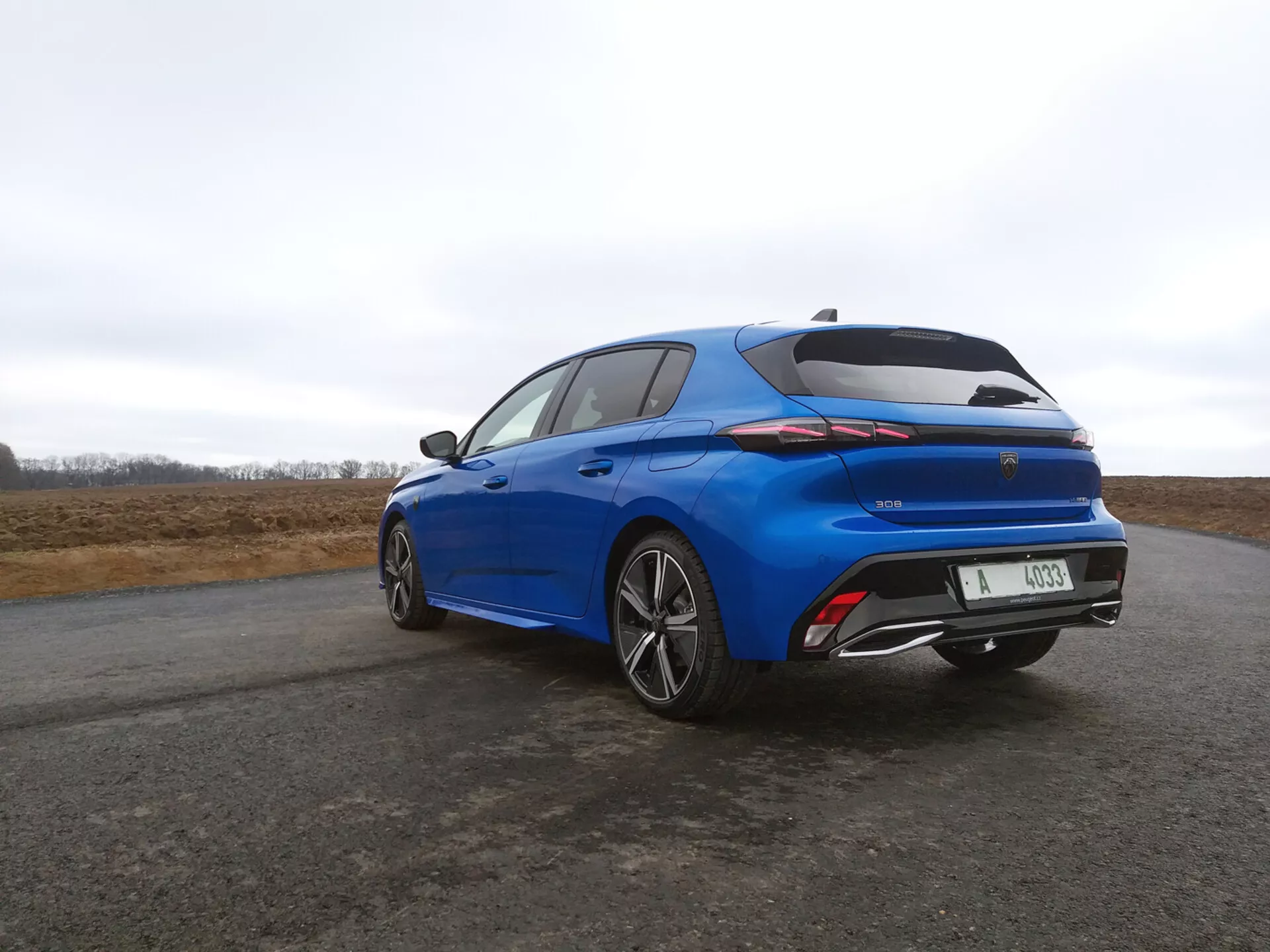 Peugeot 308 hatchback 2022 en bleu vibrant, vue arrière trois quarts mettant en vedette des feux arrière LED, un aileron intégré et des jantes alliage à multiples branches contre un ciel couvert.