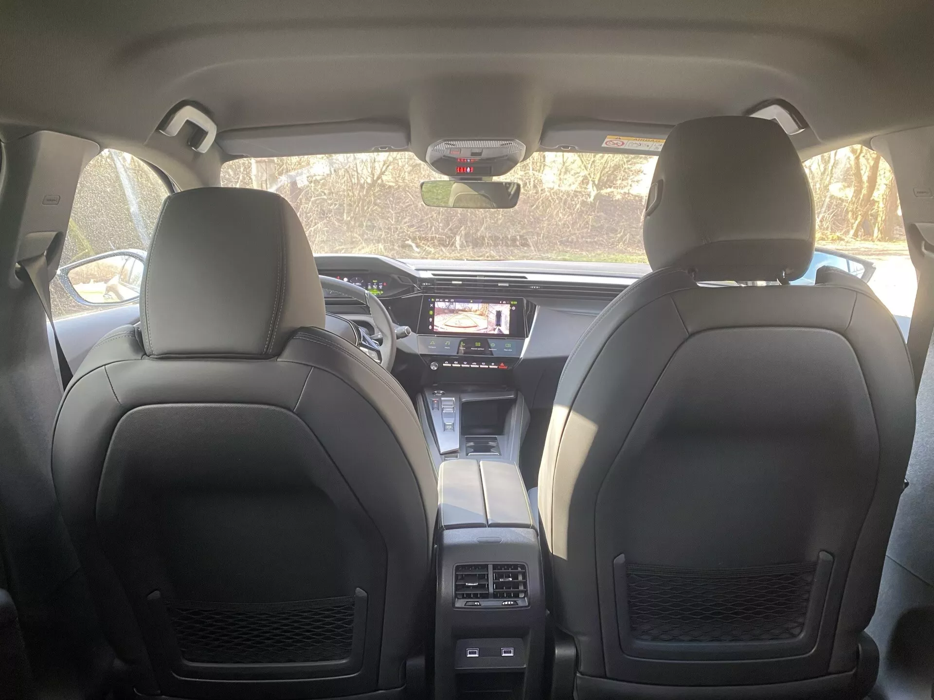 Vue intérieure de la Peugeot 408 2023 montrant le tableau de bord, les sièges avant en cuir et la console centrale du point de vue du siège arrière, indiquant des systèmes avancés d'infodivertissement et de contrôle climatique